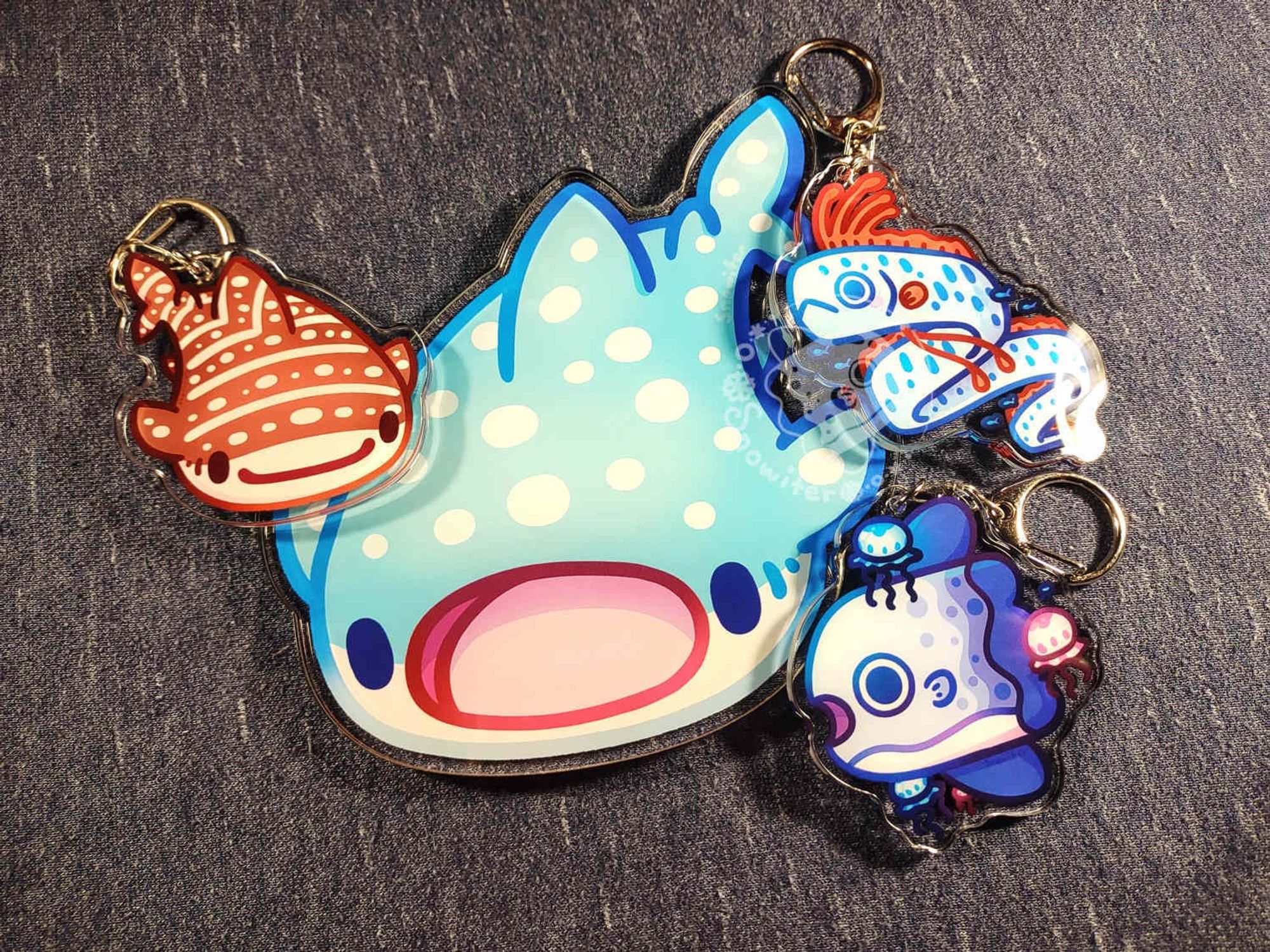 A whale fish coaster surrounded by a whale fish, mola and oarfish keychains.