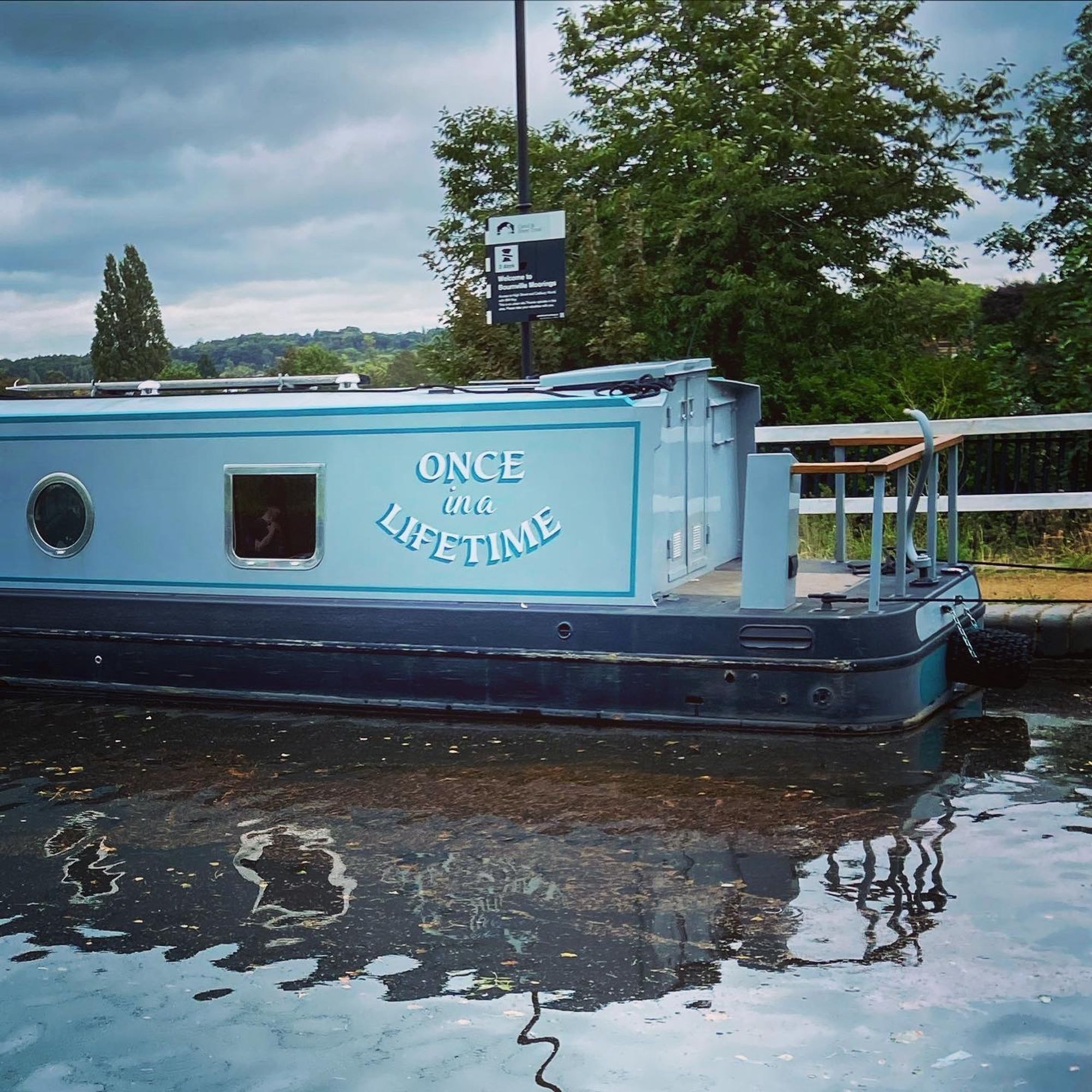 photo of a canal with a blue longboat. the name "once in a lifetime" is painted on the side