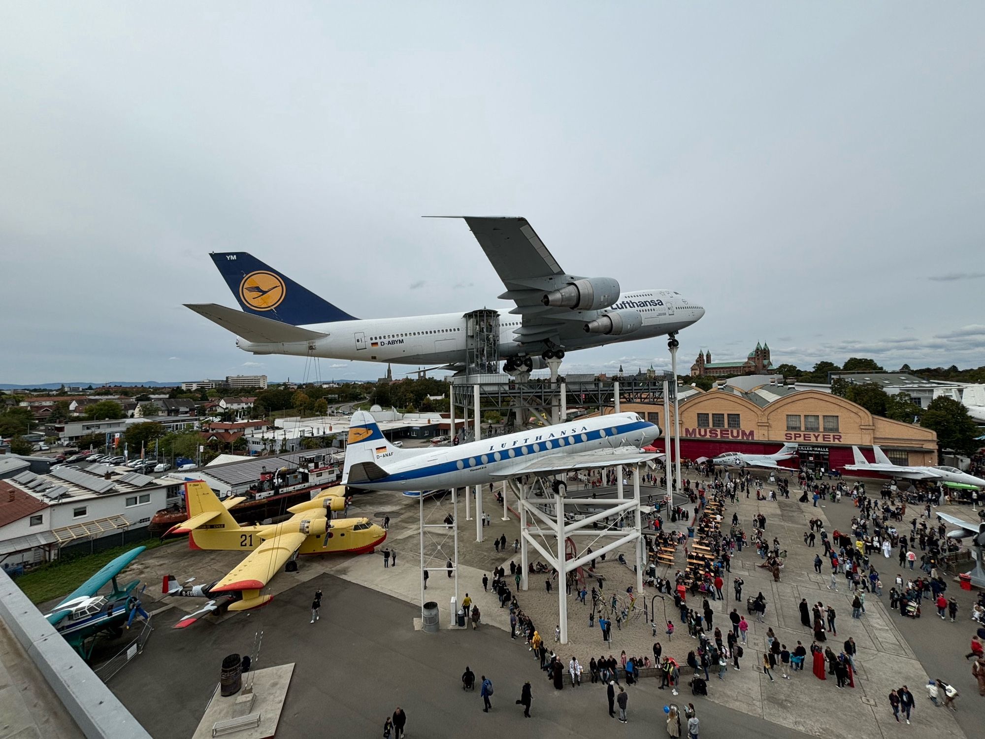 Foto vom Dach der Raumfahrt-Halle aus auf den Platz vom Technikmuseum mit aufgebockten Flugzeugen und vielen Menschen die herumwuseln.