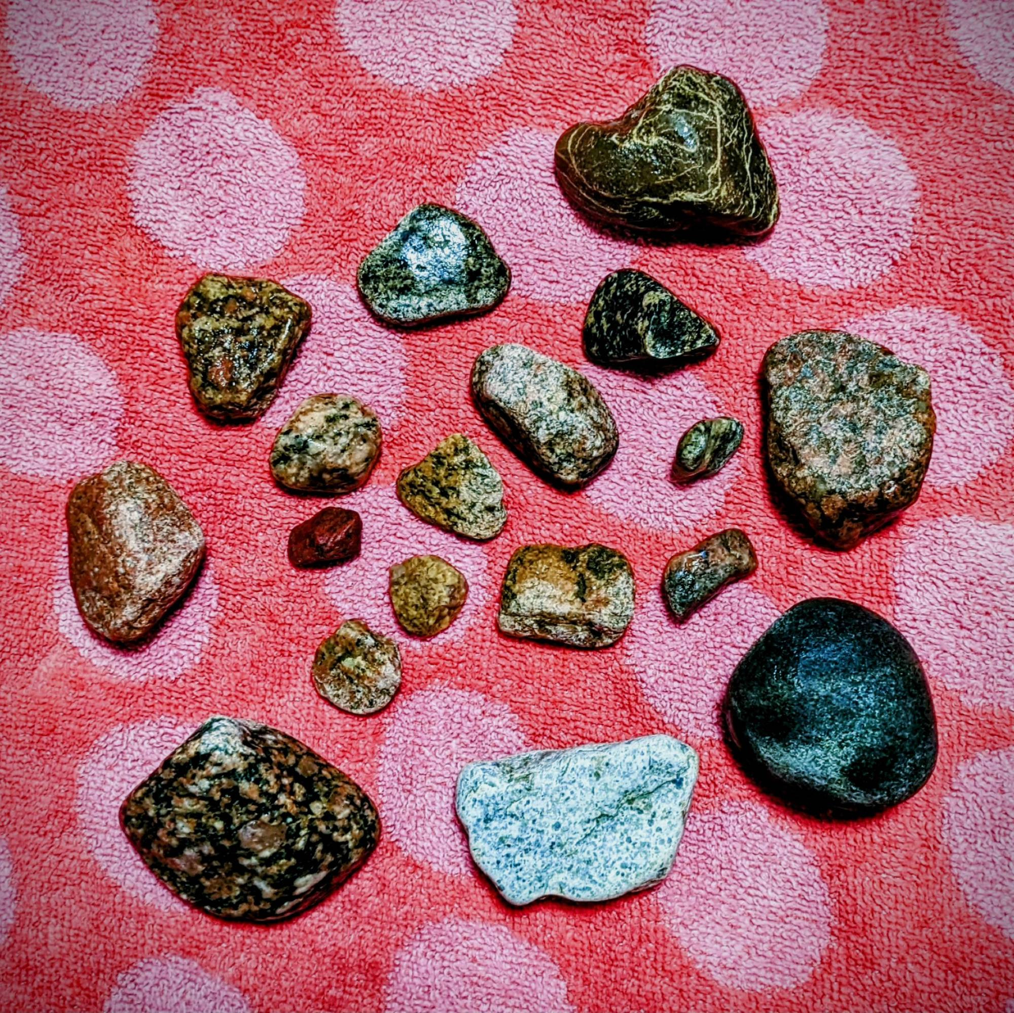 Eighteen rocks found on a riverbank, spread out over a red towel with pink polka dots. Each rock varies in size, shape, type, and color.