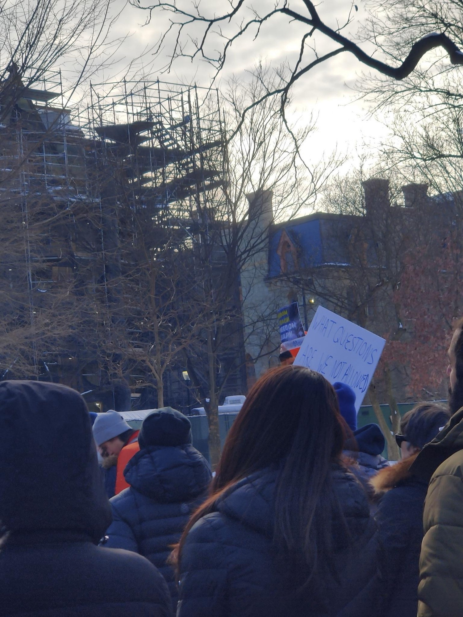 A sign held by a student asks: “What questions are we not allowed to ask?”