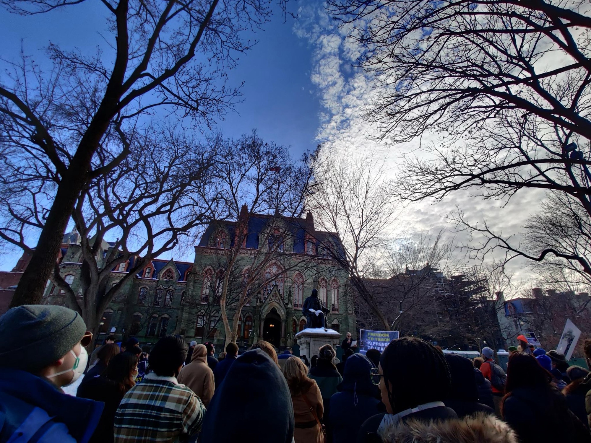 Large crowd gathers in the snow in front of a statue of Benjamin Franklin. One sign reads: “Freedom to Teach is Freedom to Learn.”