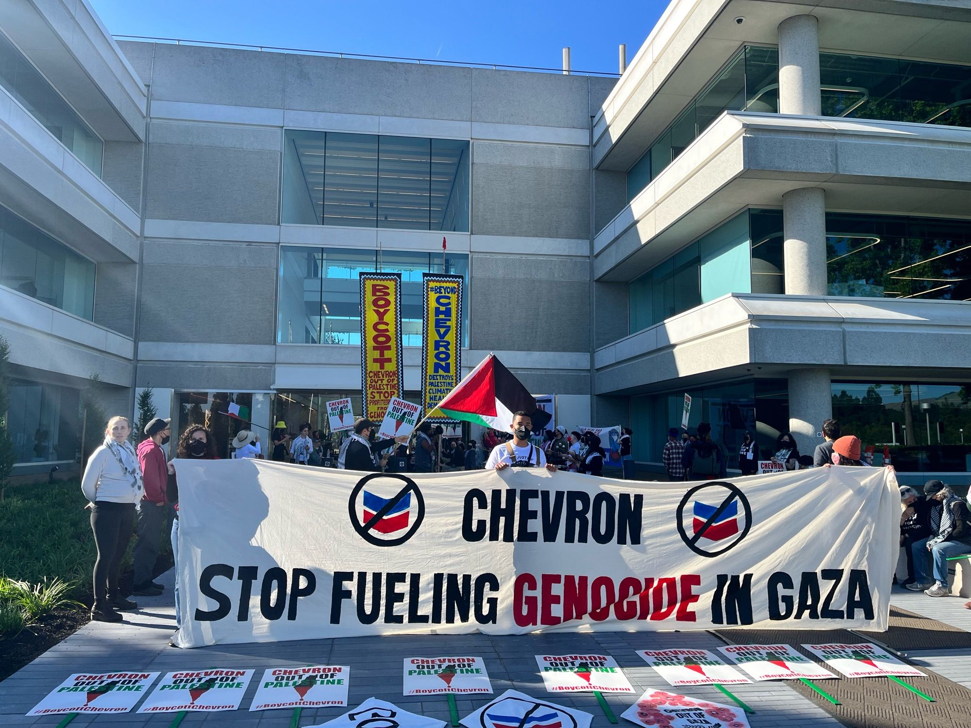 Photos of protestors outside a building. A Palestinian flag is being waved and a banner reads “Chevron stop fueling genocide in Gaza”