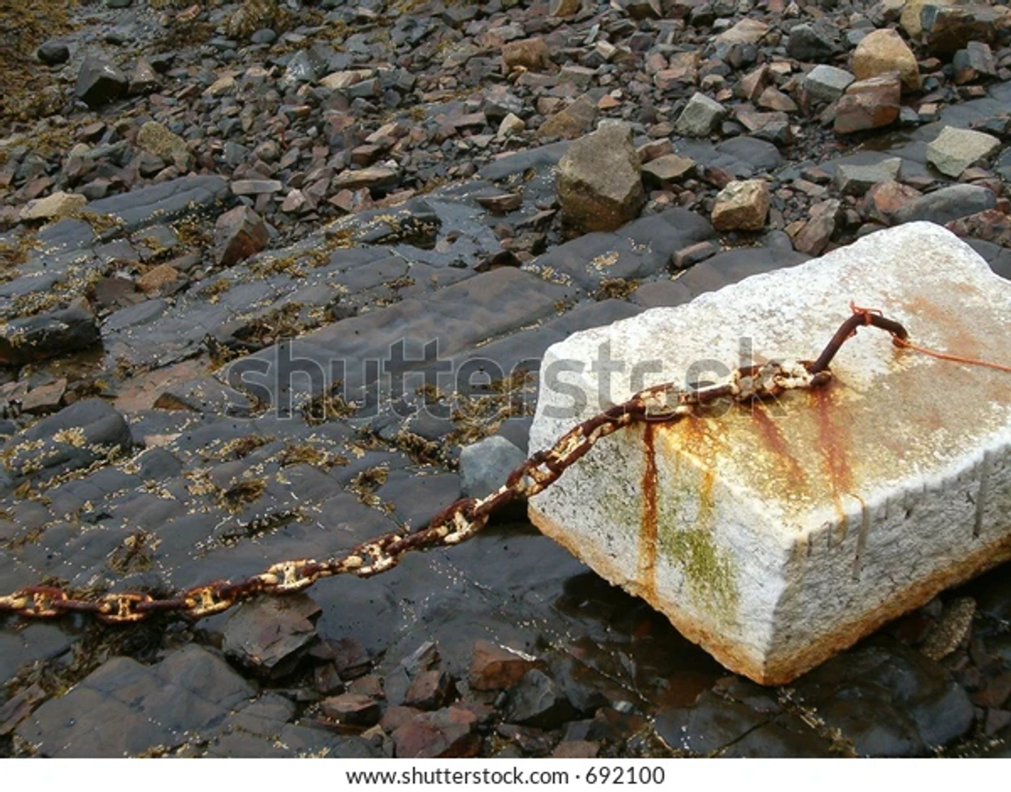 A rusty chain attached to a concrete block. Which is also somehow rusty.