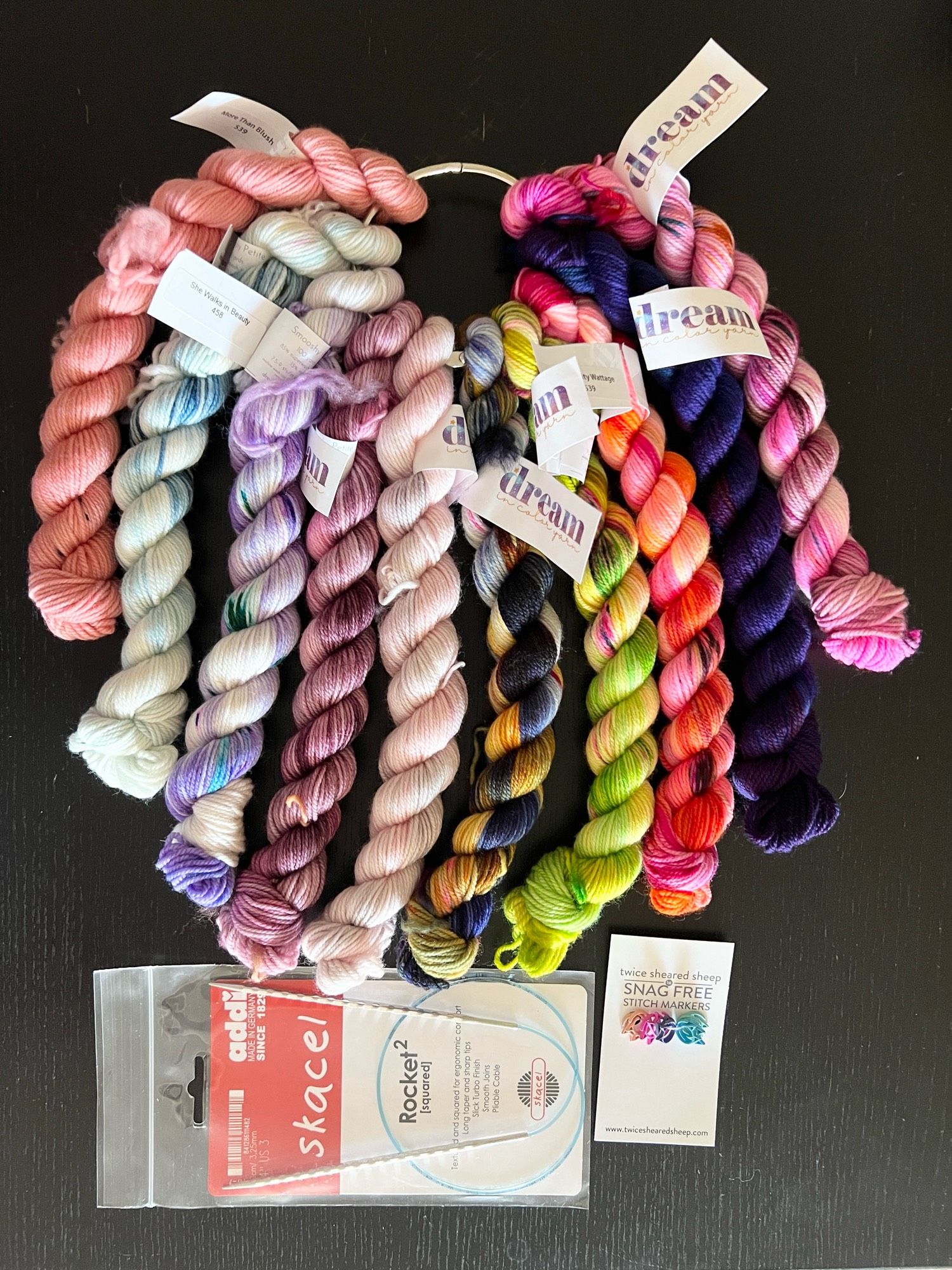 A photo of ten dream in color mini skeins of yarn plus an addi rocket circular needle and some cat head stitch markers