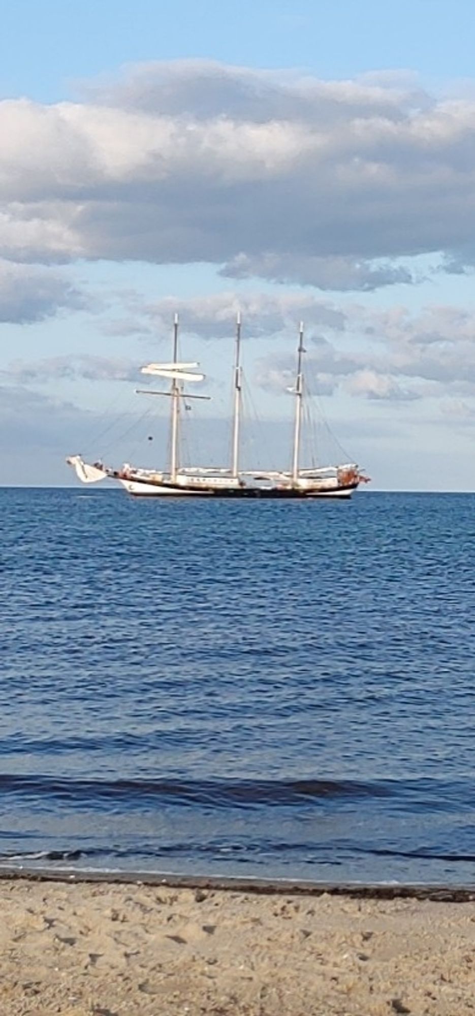 Dreimaster, der ziemlich dich vor einem Strand ankert.