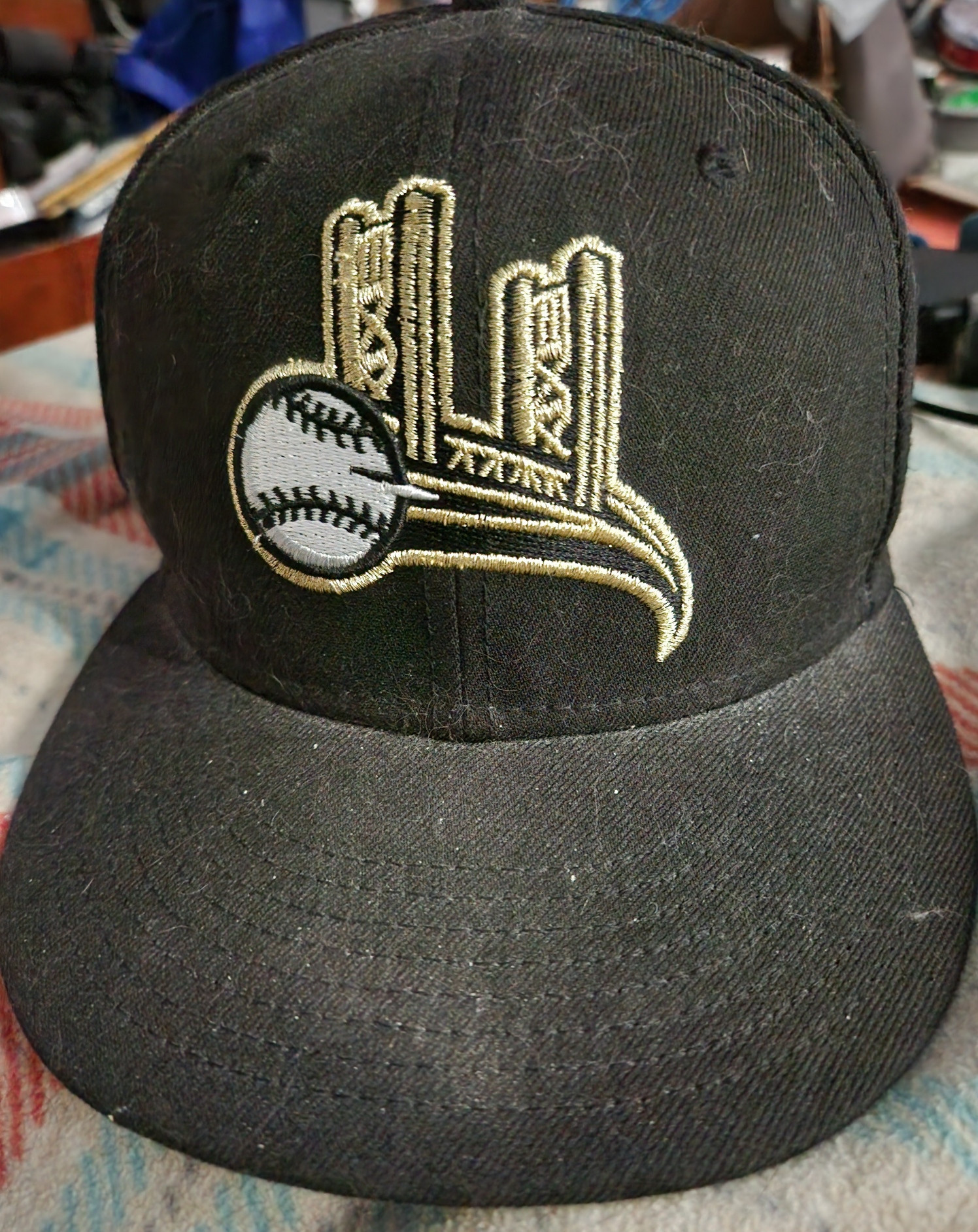 A Sacramento Rivercats alternate baseball cap, showing the Tower Bridge with its deck being a flying baseball. The cap is black and the emblem is in gold with a white baseball.