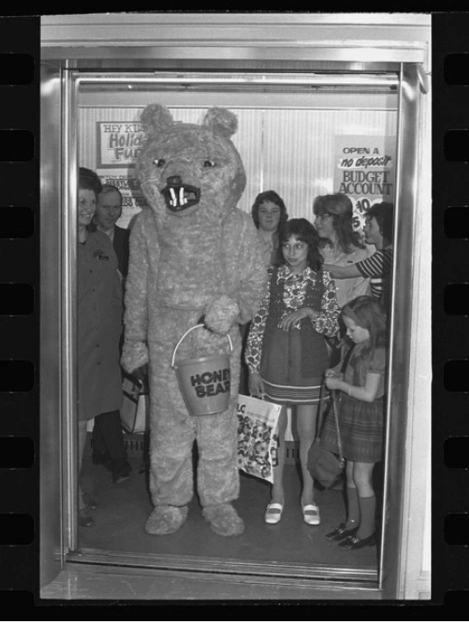 a bear with extremely fucked teeth carrying a bucket full of honey. Children eye it warily.