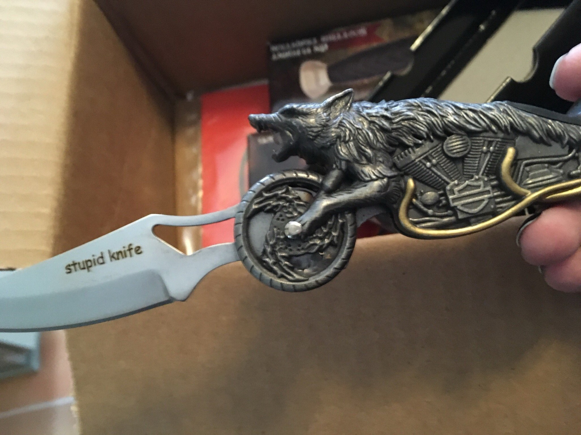 A photo of a dumb BudK knife with a handle in the shape of a motorcycle/werewolf hybrid. The blade is helpfully engraved with “stupid knife” in comic sans.