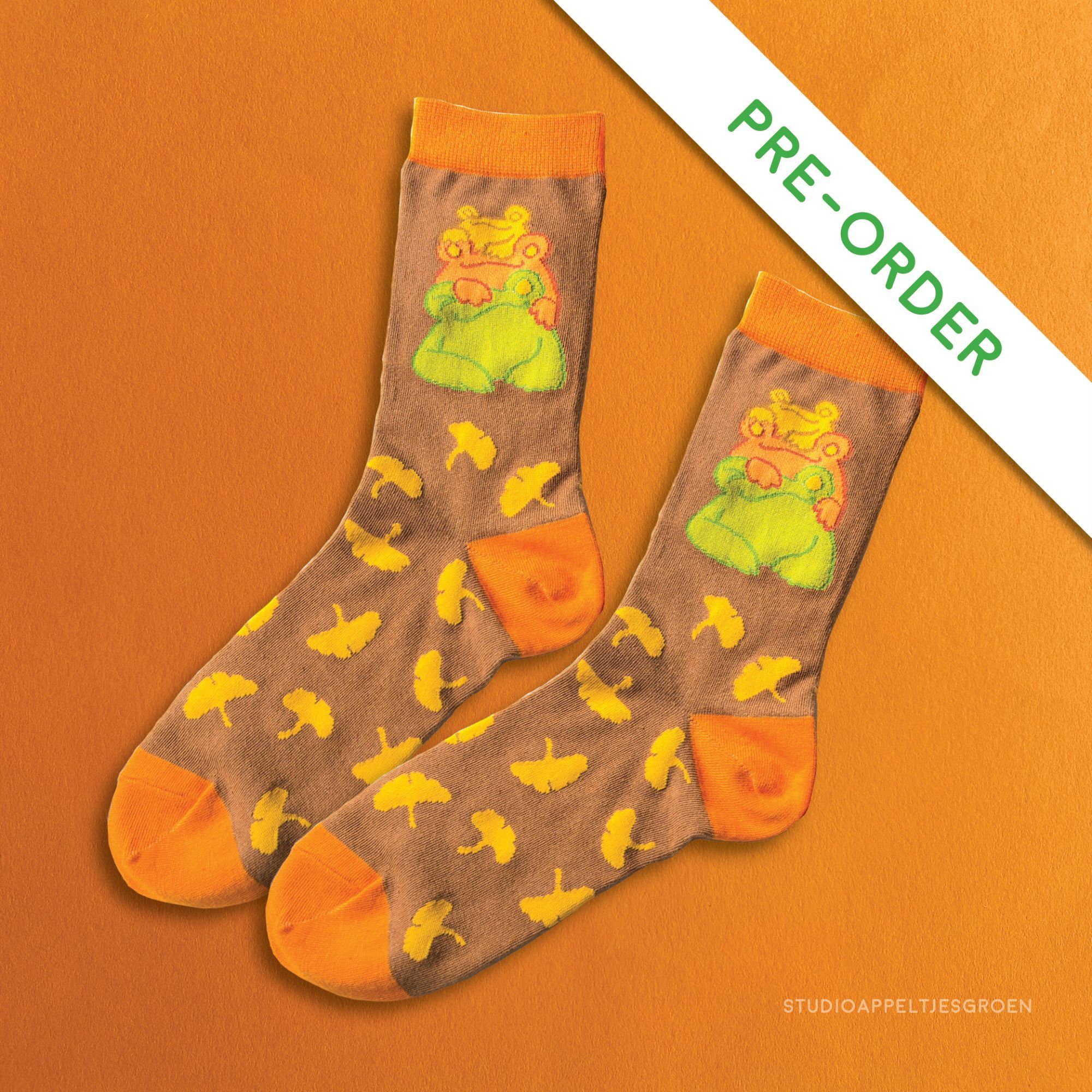 Orange and brown socks with a gingko leaves pattern with three frogs stacked on top of each other looking happy.