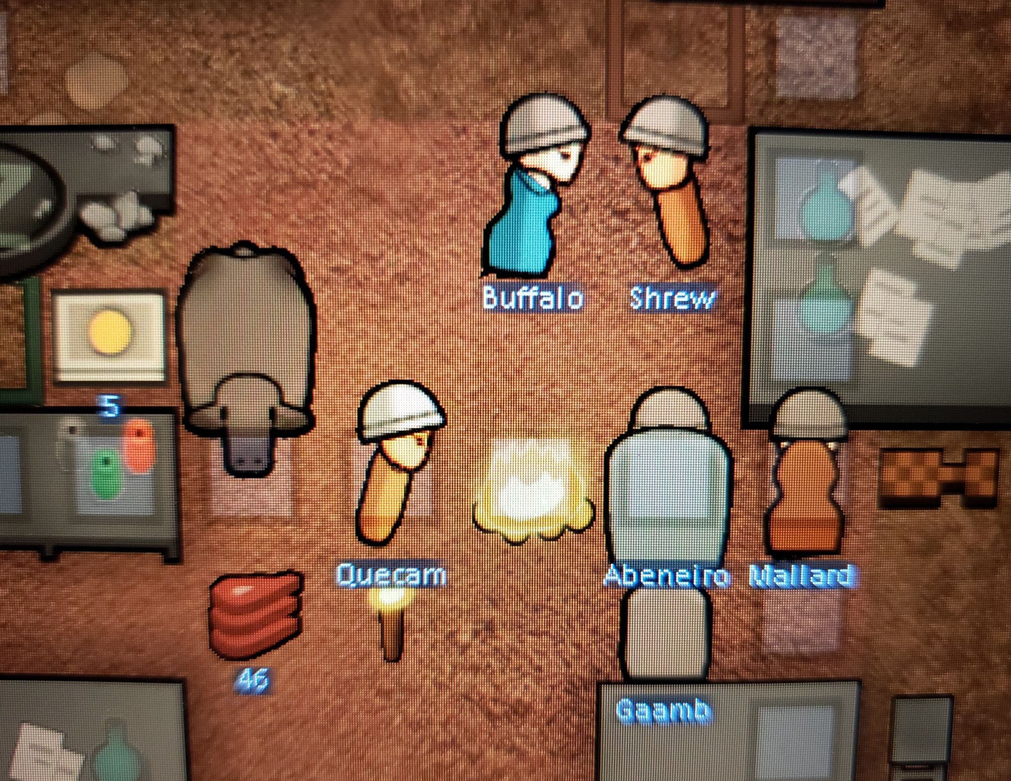 Six rimworld characters in a room surrounded by random items including a campfire, a boardgame, several metal tables, a pile of meat, and a yak