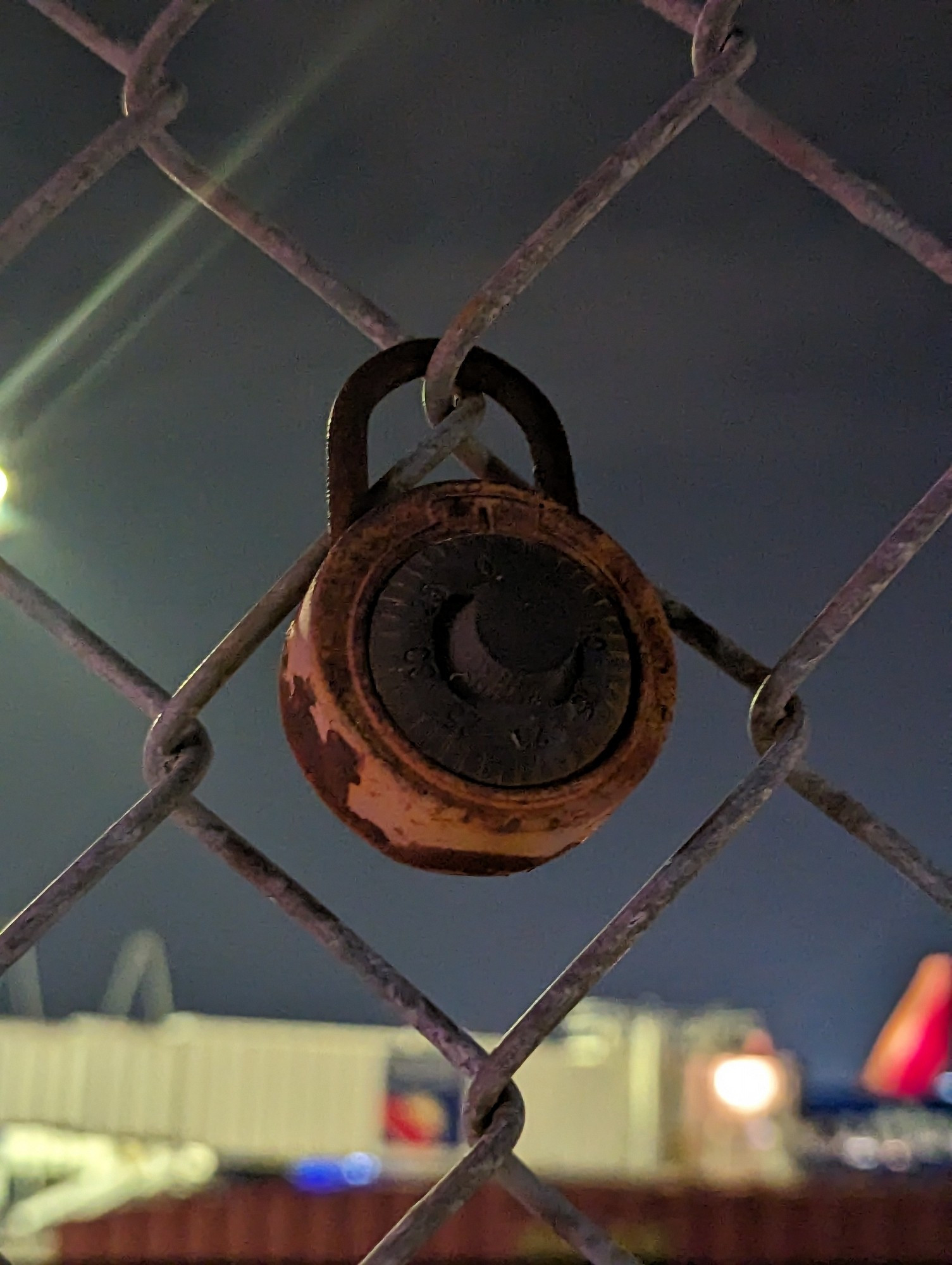 A rusted lock on a chain link fence.