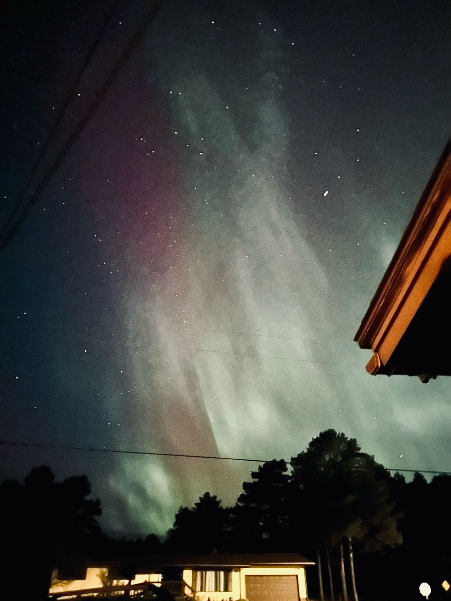 Photo of the sky with the northern lights above a yellow house, the northern lights are purple, blue, green, and white