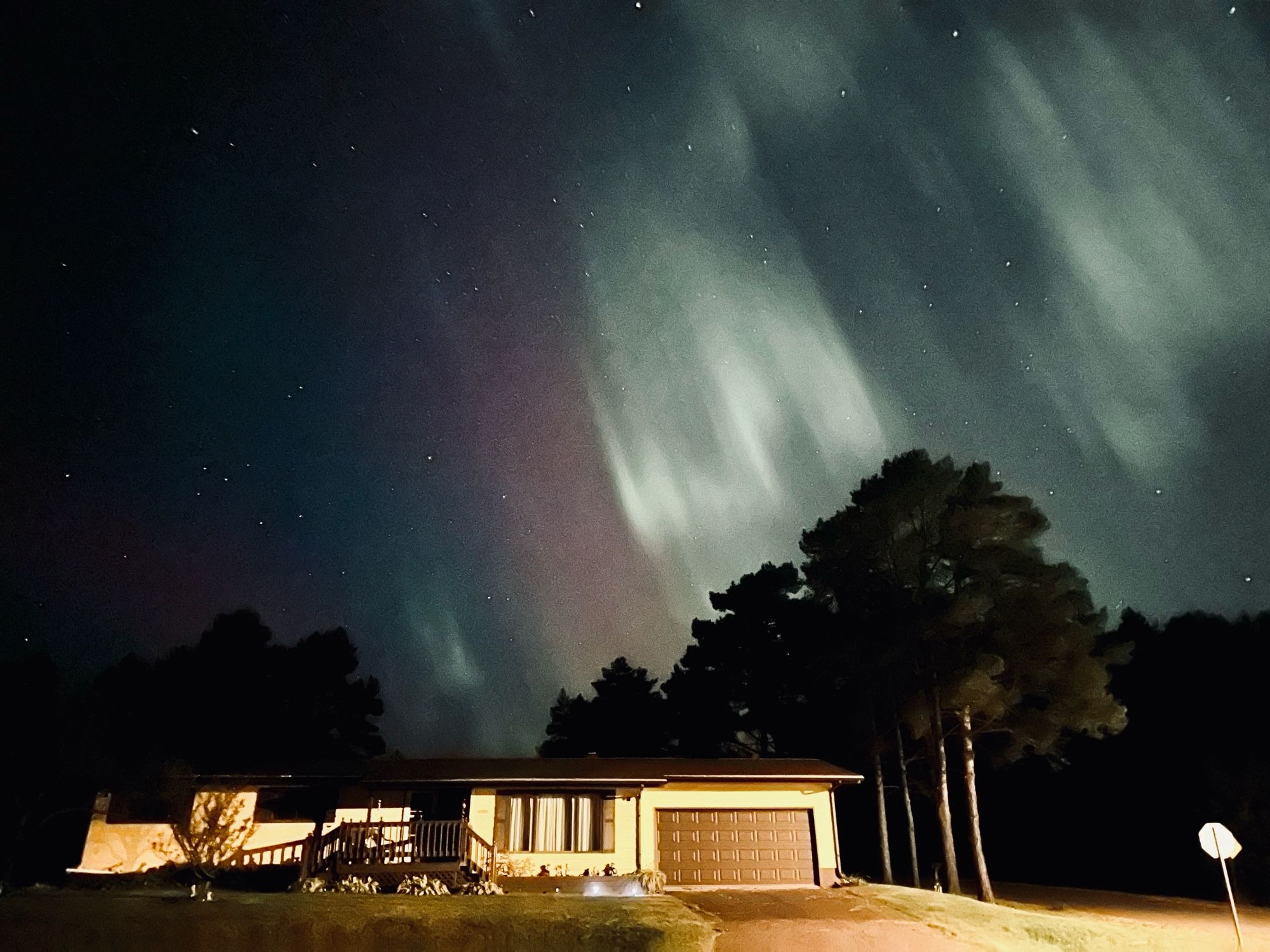 Photo of the sky with the northern lights above a yellow house, the northern lights are purple, blue, green, and white