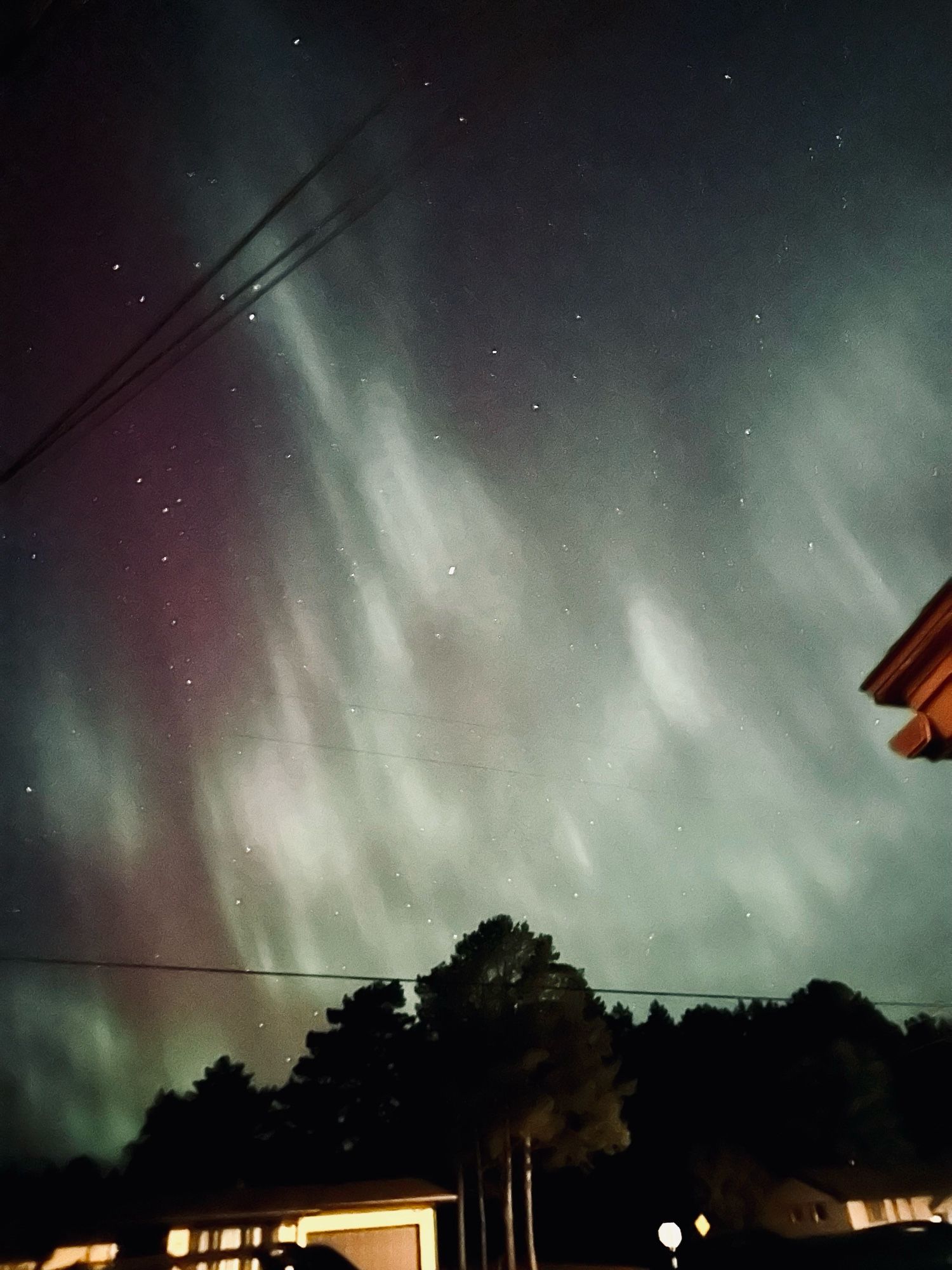 Photo of the sky with the northern lights above a yellow house, the northern lights are purple, blue, green, and white