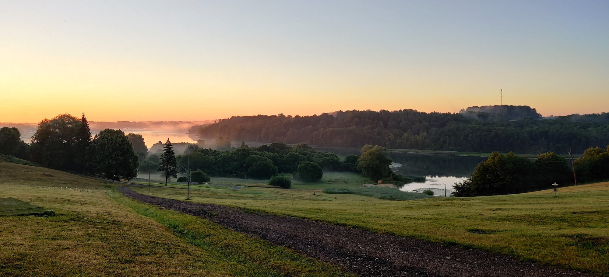 Photo of a sunrise over a lake in a small valley. There is a path going down the hill.