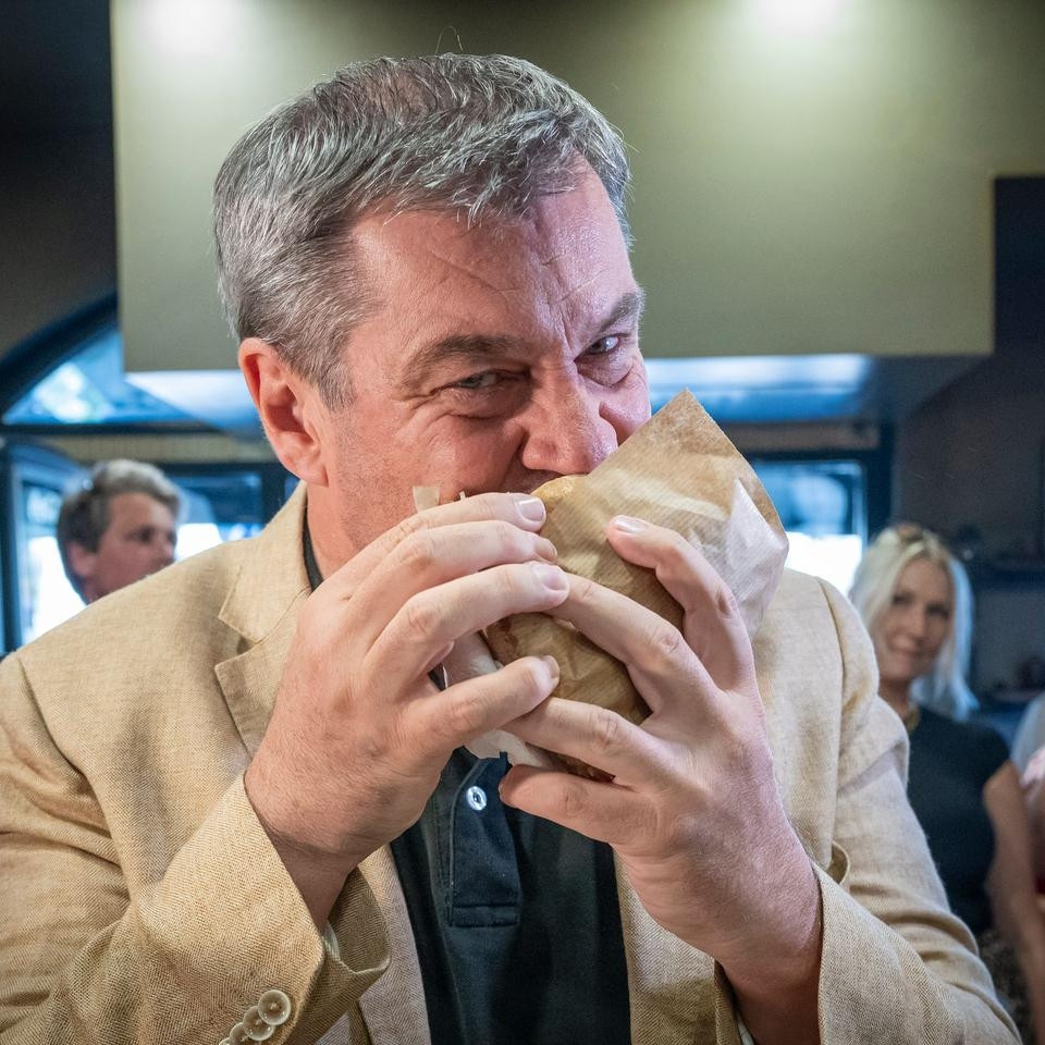 Söder frisst Döner mit hochrotem Gesicht.
