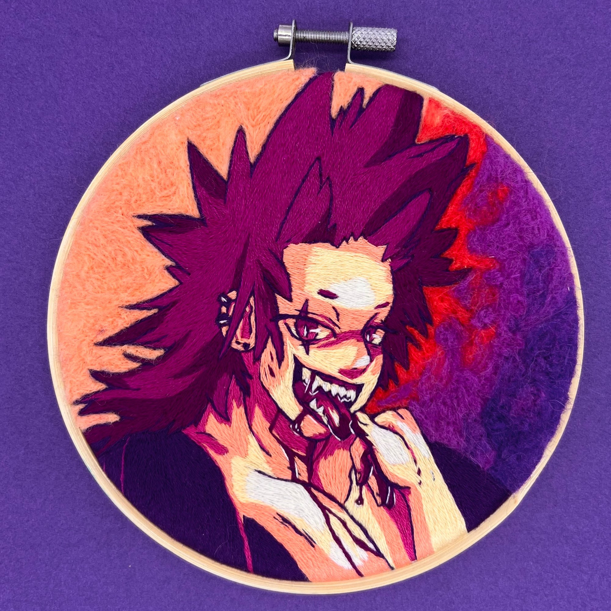 A hand embroidered hoop of the character Kirishima from My Hero Academia on a purple background. He’s stitched in a pink and orange color pallet with a background made of purple, red, and orange needle felted wool. A small splatter of blood is scattered across his body, face, and arm. He’s looking towards the viewer while licking off blood from his fingertips.