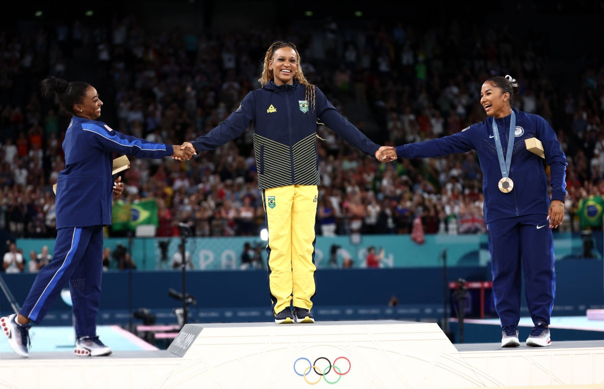 On the podium for the women's floor exercise, gold medalist Rebeca Andrade takes the hands of Simone Biles (silver) and Jordan Chiles (bronze) after Simone and Jordan bowed down to Rebeca. Such a lovely scene!