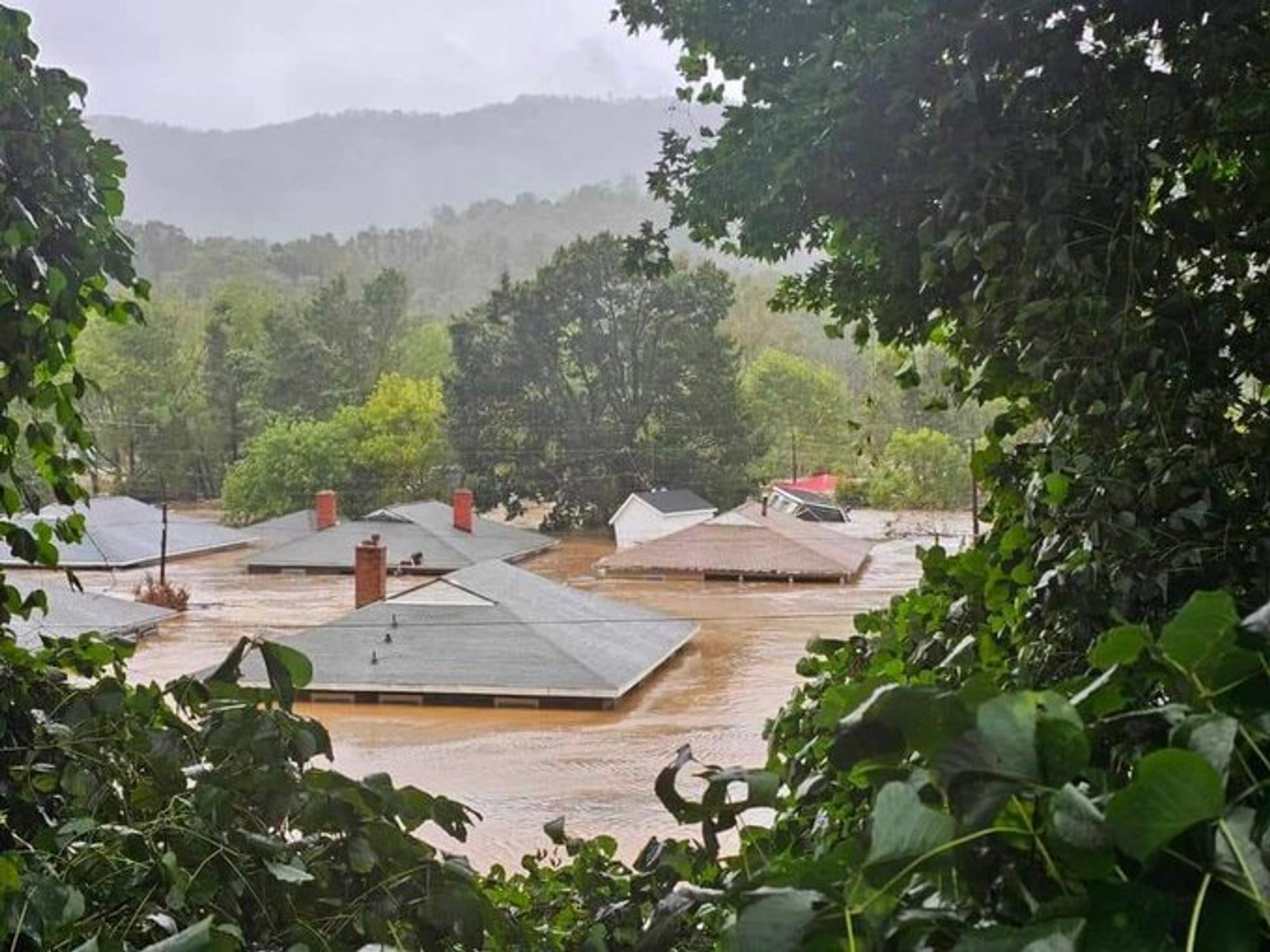 Swannanoa river flood engulfing various houses submerged to the roof level. A person can be seen sitting on one of the roofs.