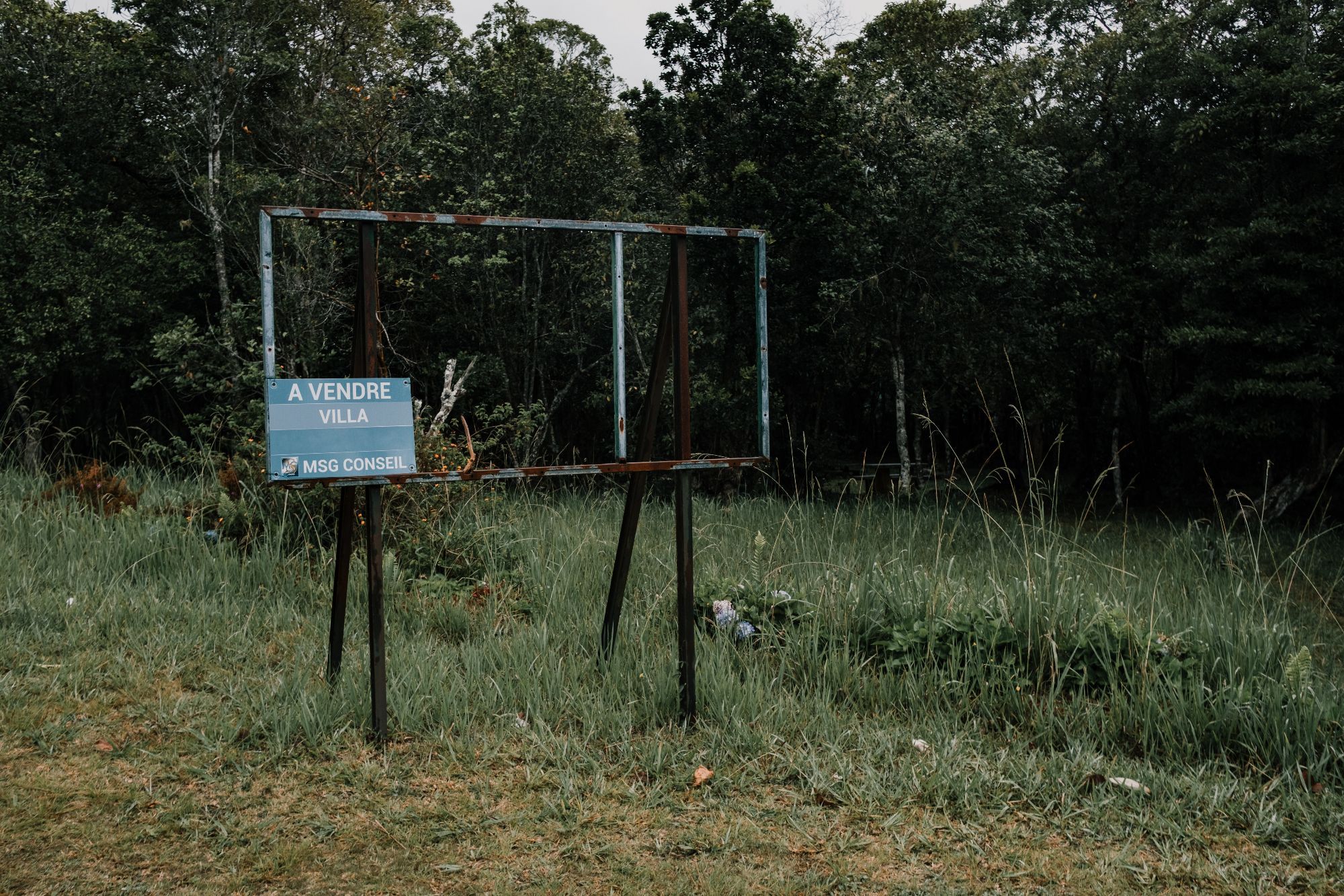 Un panneau "a vendre villa" vide présentant un cadre dans le cadre rempli d'arbres.