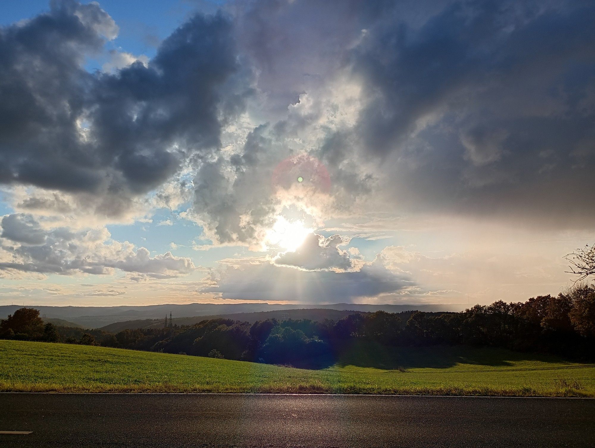 Beautiful view with green nature, a cloudy sky and the sun.