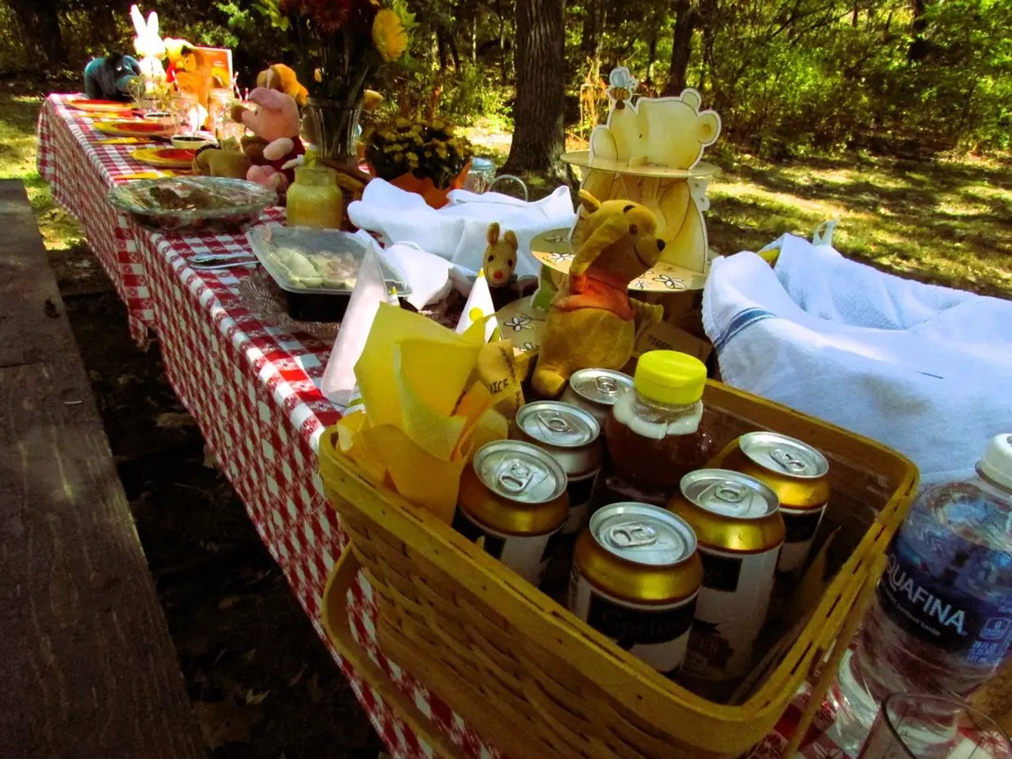 Another angle of the picnic table. There is a basket in the foreground filled with ginger beer and a Winnie the Pooh beanie plush.