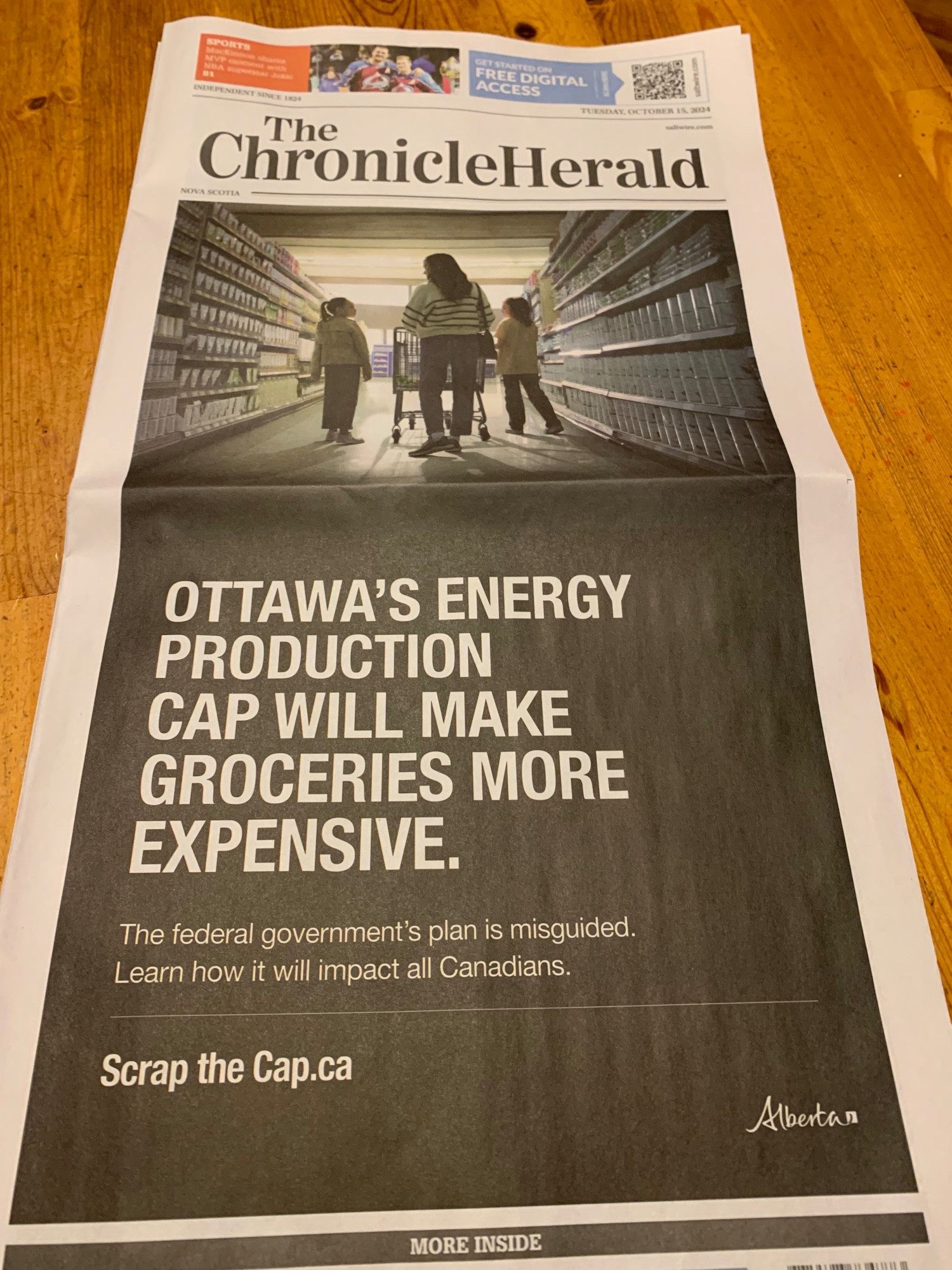 The entire front page of the Chronicle Herald is an ad. The ad is a photo of a woman and two children in a grocery aisle. Beneath reads "Ottawa's Energy Production Cap Will Make Groceries More Expensive. The federal government's plan is misguided. Learn how it will impact all Canadians. Scrap the Cap.ca Alberta"