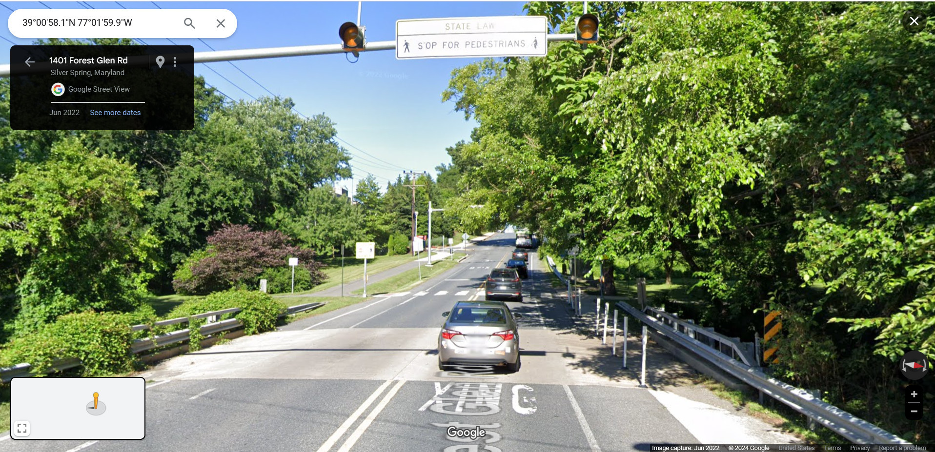 Google Streetview of a two-lane road, approaching a trail crossing. There is Ped Xing stenciled on the pavement. There are overhead flashing lights with an overhead sign that says "state law, stop for pedestrians". There are stop bars. There is a forest of signs telling drivers to stop for pedestrians. There are white plastic flexposts to narrow the perception of road width for drivers.