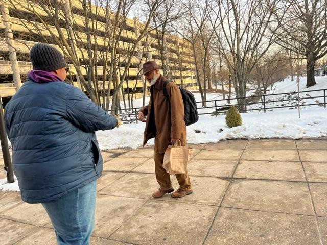 A person bundled up in winter clothing, offering a leaflet to a person also bundled up in winter clothing, on the lower side of the Shady Grove Metro station.