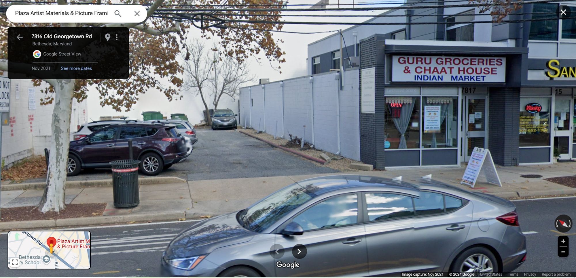 Google Streetview of a one-story building, with a white blank wall facing an alley parking lot. There are cars parked nose-in facing away from the white blank wall. There are 5 downspouts spaced along the wall. Four of the downspouts are protected from drivers by bollards.