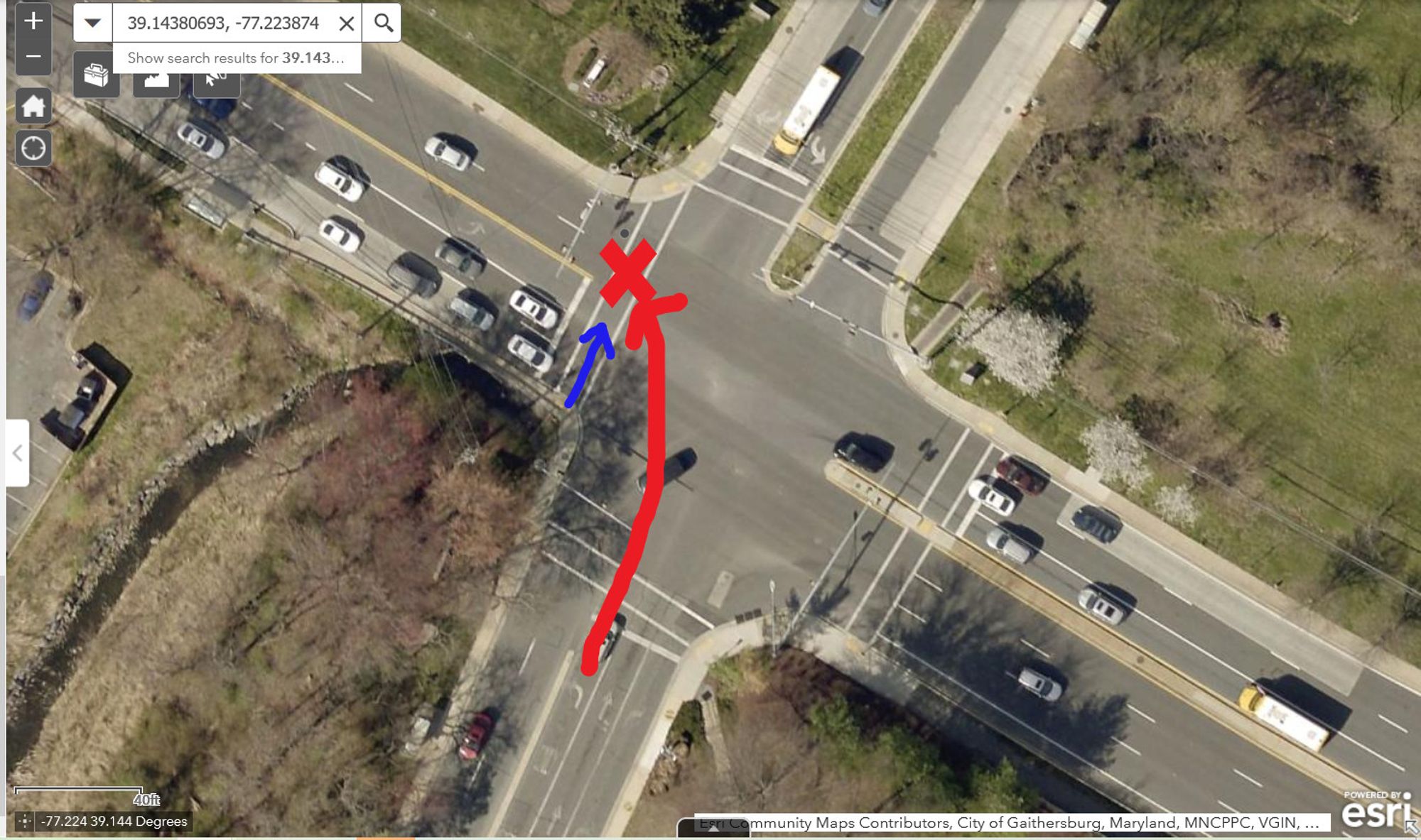 Satellite image of a large four-way intersection of two large divided roads, with traffic signals, and with four marked crosswalks, of which three are set back from the intersection. There is a red X in the west leg marked crosswalk, which is the not off set one, indicating the location of the crash. There is a red arrow indicating the path of the driver from the south leg left turn only lane towards the crash location. There is a blue arrow going north in the marked crosswalk toward the red x, indicating the path of the pedestrian.