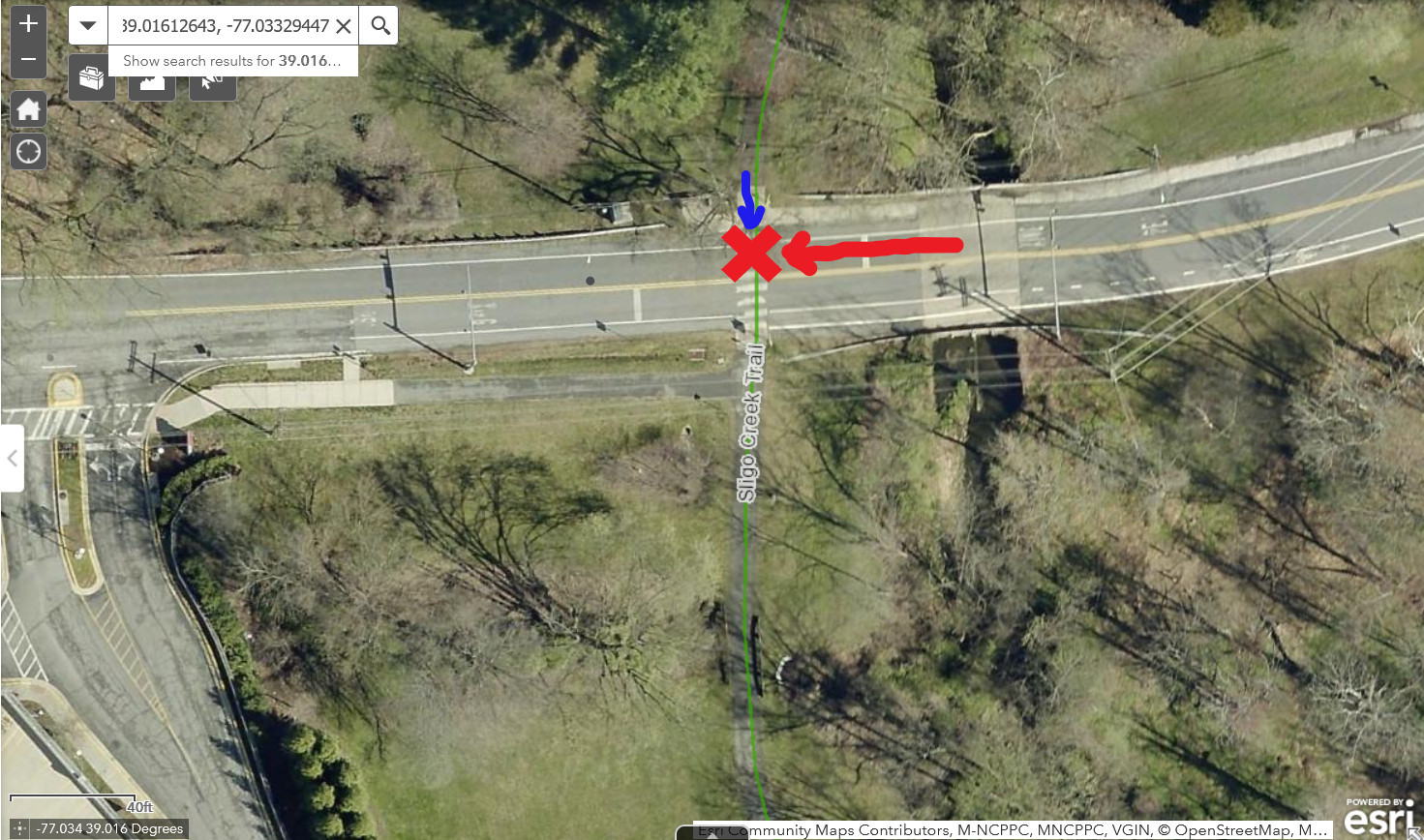 Satellite image of a two-lane road with a marked crosswalk where the Sligo Creek Trail crosses the road. There are stop bars set back in the road on for drivers from both directions. There is a red X in the marked crosswalk on the north side of the road, indicating the location of the crash. There is a red arrow pointing left toward the red X, indicating the path of the driver going west. There is a blue arrow pointing south toward the red X, indicating the path of the child going south on the bike path.