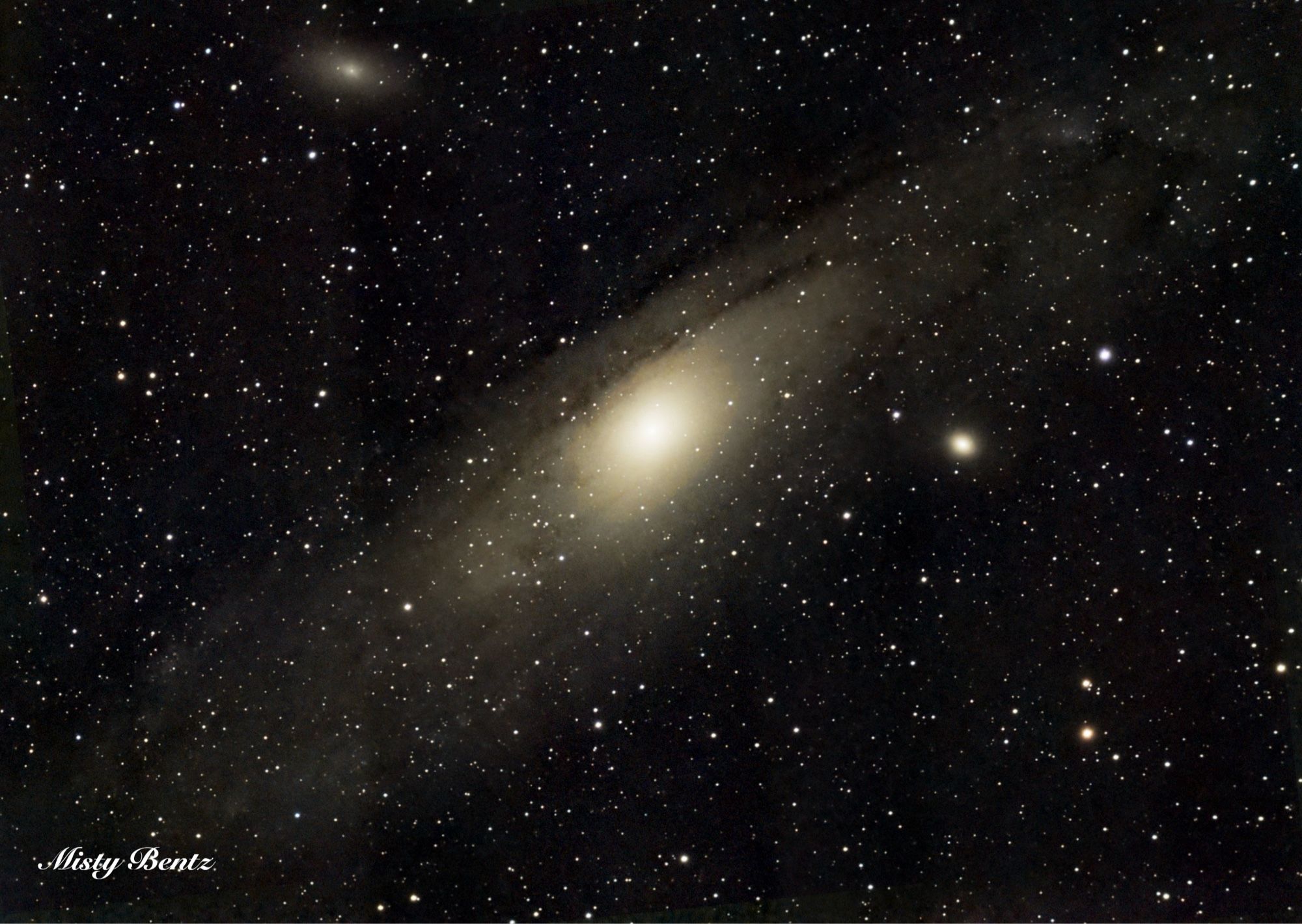 A large bright yellowish spiral galaxy with brown dust lanes running around the edge of the disk and a bright center. A few smaller spheroidal galaxies are located nearby, and the large galaxy is centered on a black background dotted with stars, but tilted so that it runs from bottom left to top right