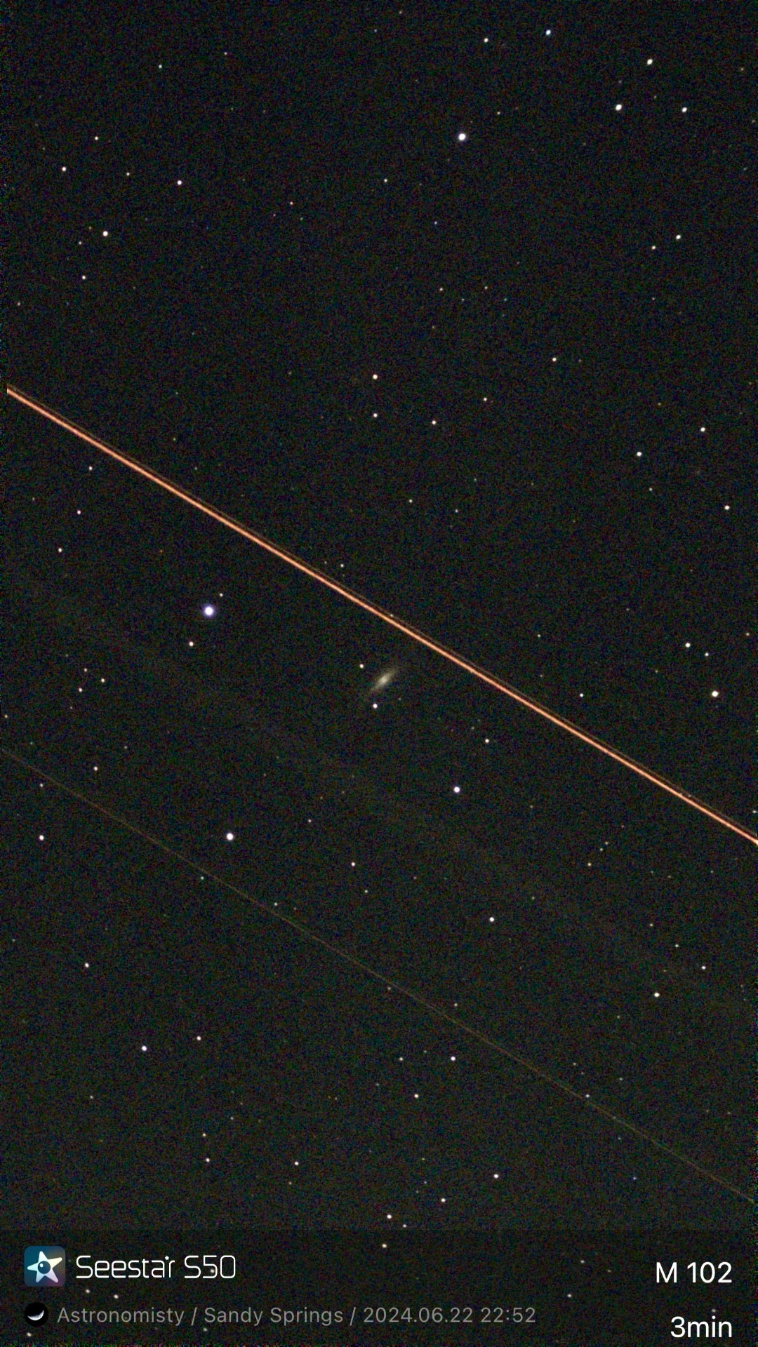 Faint image of a galaxy from my Seestar S50 telescope with a bright red diagonal streak across the frame and some fainter parallel streaks below.