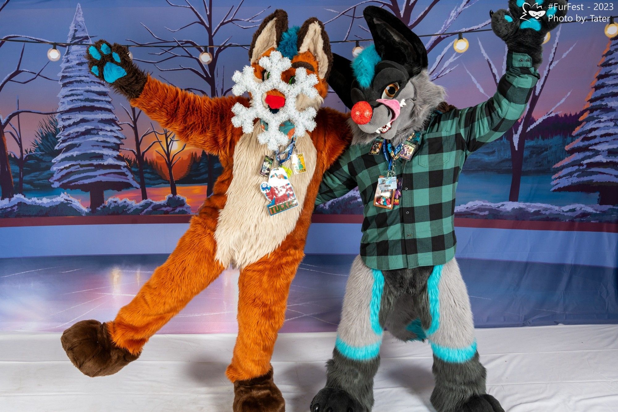 Two fox fursuiters being goofy. The one on the left has a snowflake on his snoot, and the other is wearing a red nose