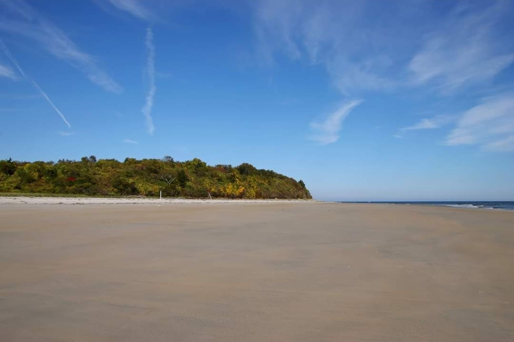 A wide expanse of sand with a dune covered in vegetation in the background. A little of the sea on the right. It all meets a vibrant blue sky.