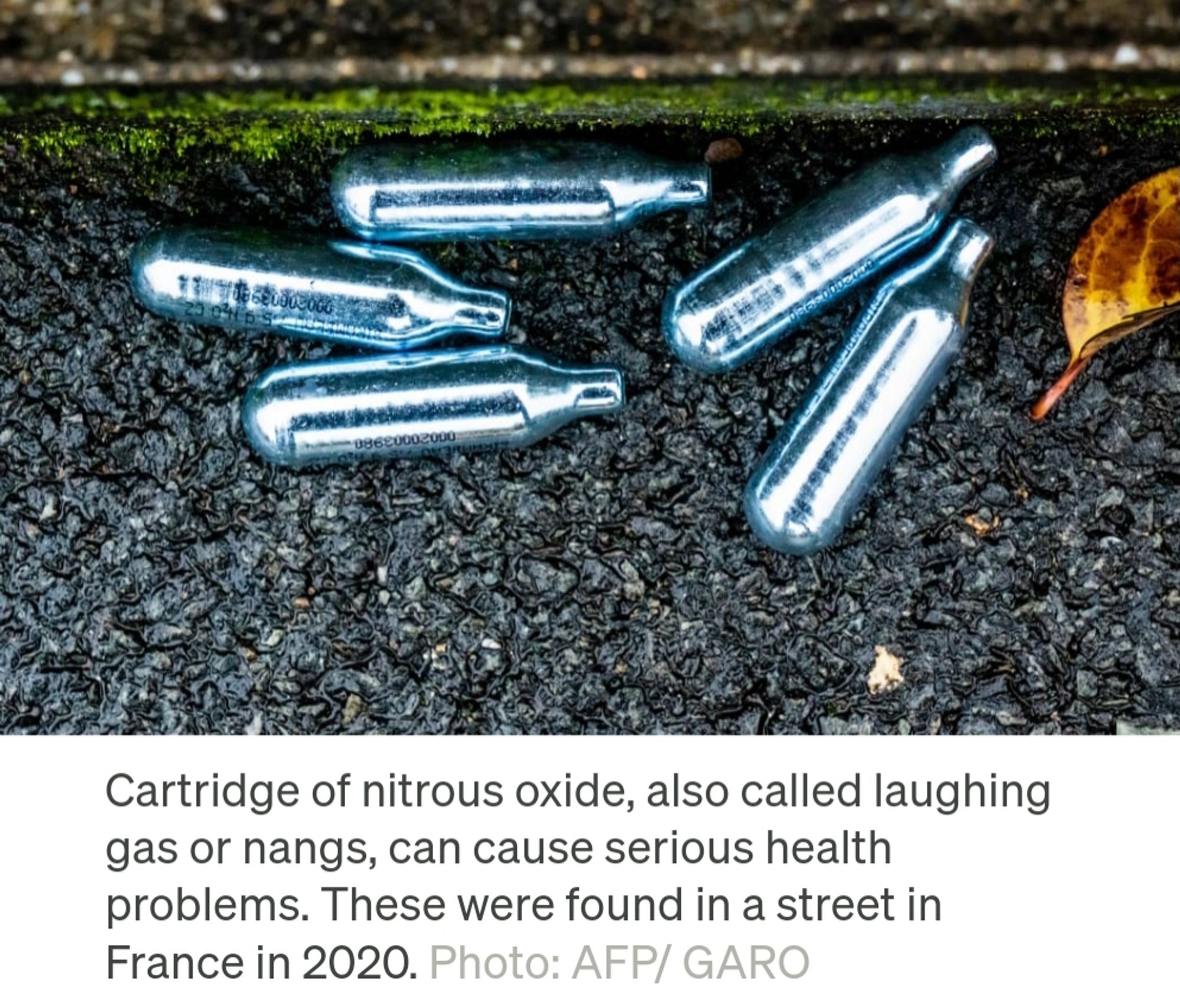 A screenshot of a photo of 5 nitrous oxide canisters lying in a gutter. The caption reads "Cartridges of nitrous oxide, also called laughing gas or bangs, can cause serious health problems. These were found in a street in France in 2020. Photo: AFP/GARO"