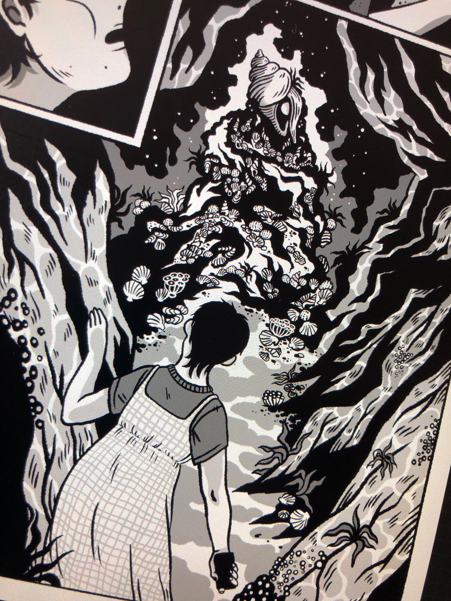 A black and white panel from the short comic I’m working on. The character is in a cavern by the sea and discovers a weird seashell.