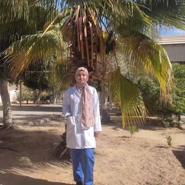 Photo of Layla, she stands in front of a palm tree and wears a lab coat.