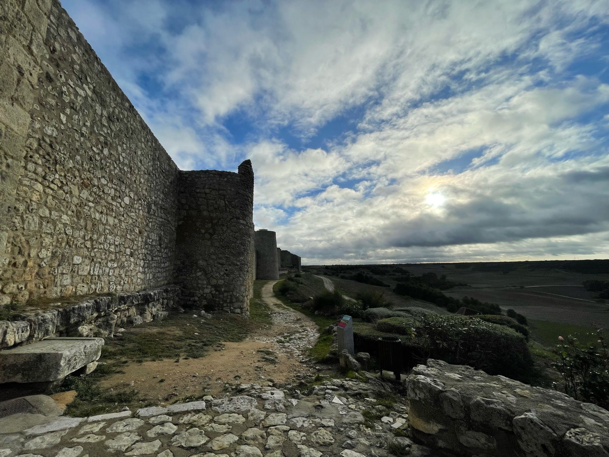 Las murallas medievales de Urueña, a la izquierda, sobre los campos de Castilla, a la derecha. Al fondo, entre las nubes rasgadas asoma tímidamente el sol de otoño.