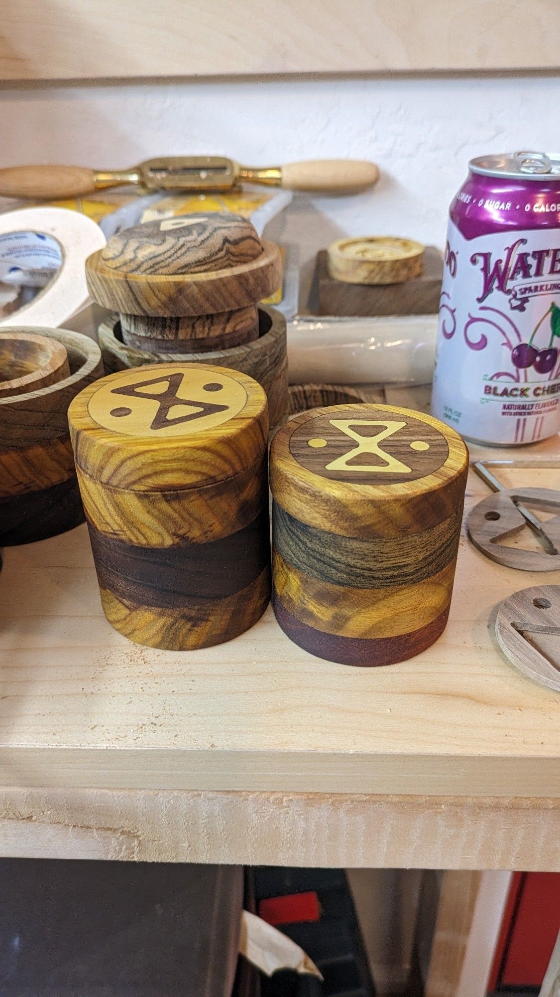 Two wooden jars made of different woods layered and lids with wood inlay of symbols that are a cross between an infinity symbol and and hourglass