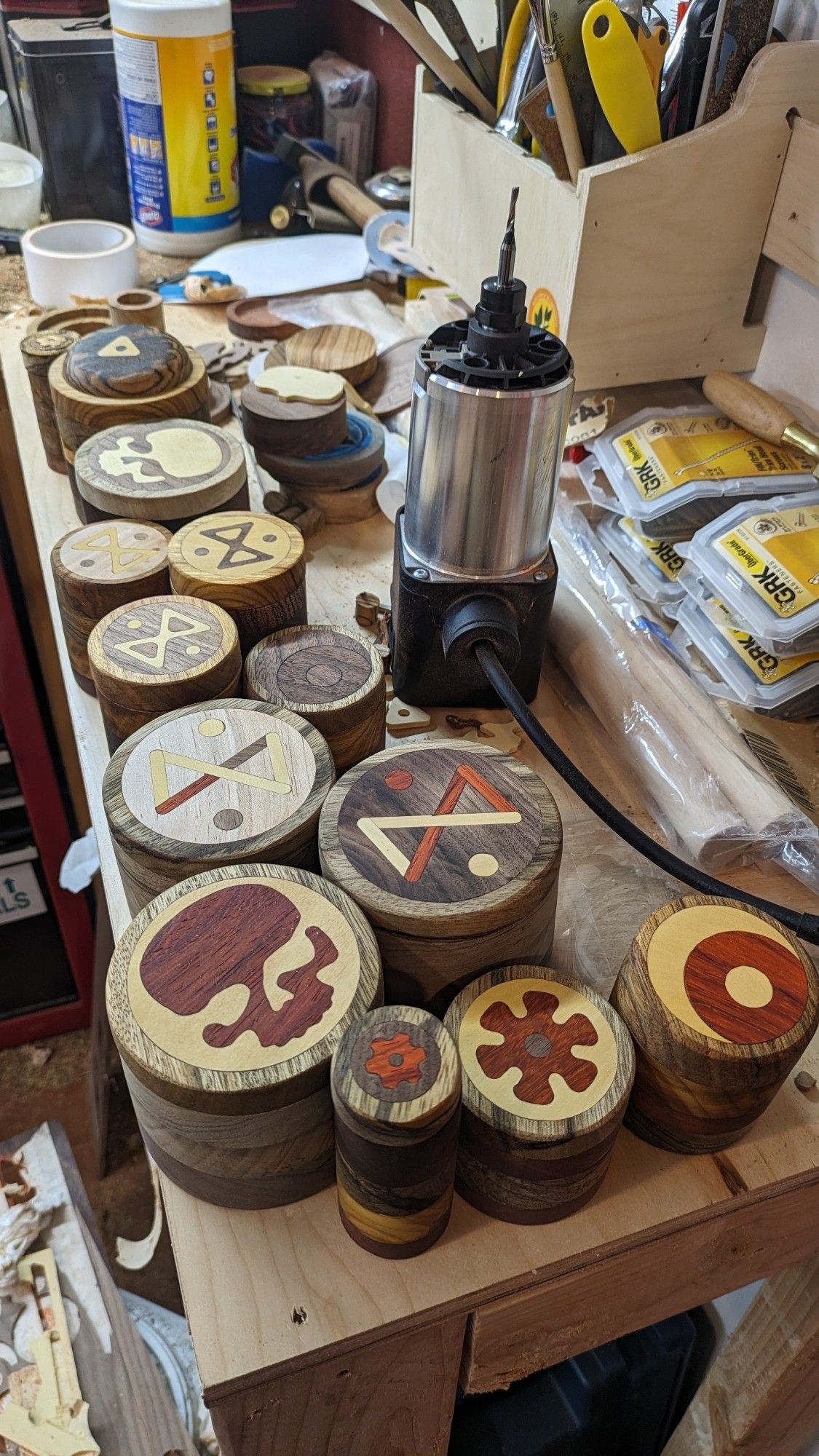 A bunch of wooden jars with various wood inlay patterns on the lid sitting on a workbench