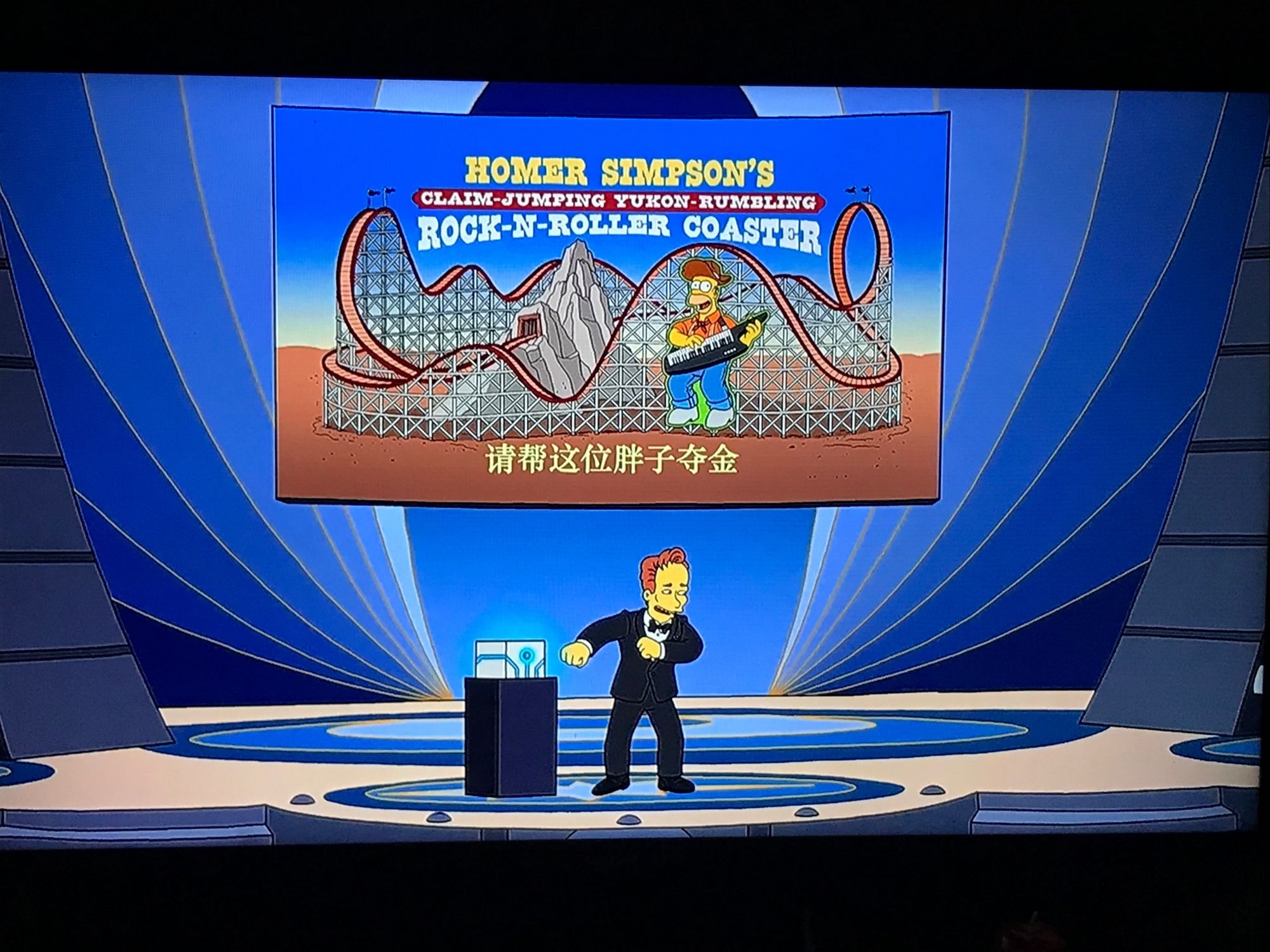 Poster above Conan O’Brien on The Simpsons season 36 episode 1, “Bart’s Birthday,” reads, “Homer Simpson’s claim-jumping Yukon-rumbling rock-n-roller coaster.”  Chinese perfectly translates on Google Translate as, “Please help this fat guy win a gold medal,” which means it may not actually be perfectly written in Chinese.  Most real Chinese doesn’t translate so perfectly on Google Translate.