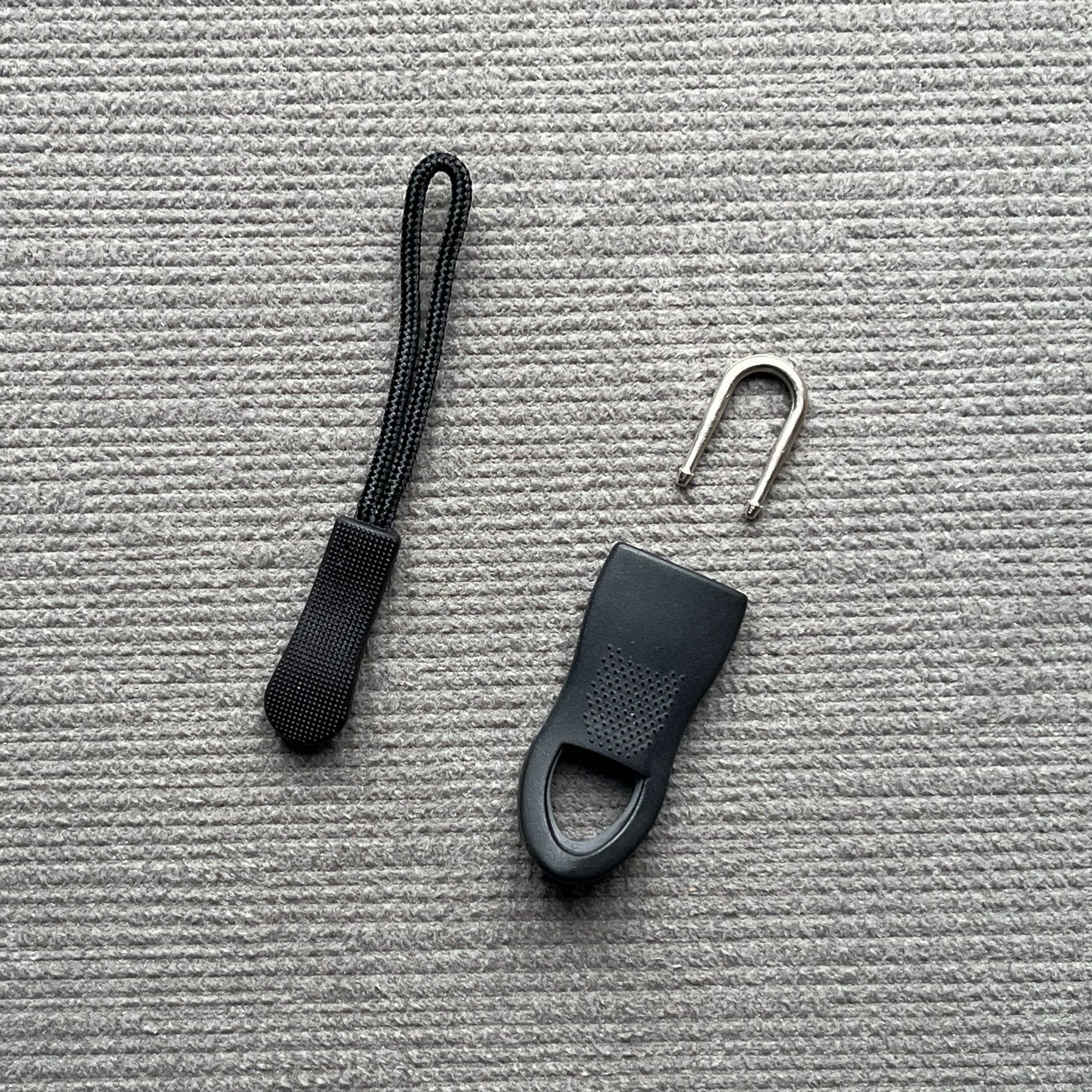 Two replacement zip pulls. On the left a narrow fabric loop with plastic pull. In the right a two part model with a metal U-hook which slots j to the wide plastic pull.