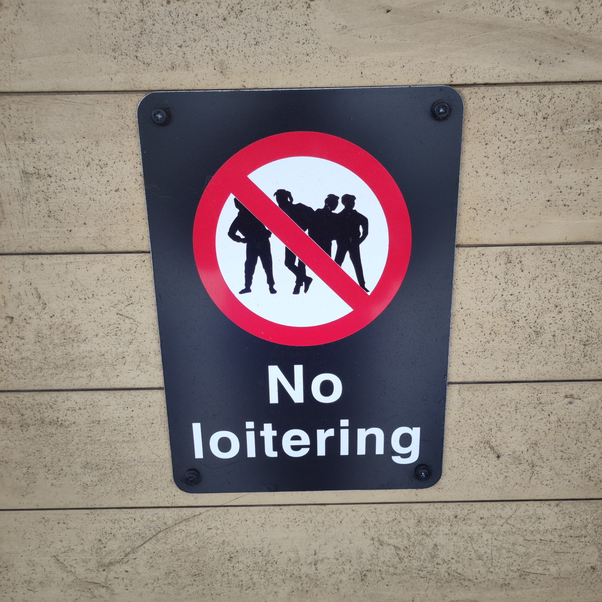 A sign for NO LOITERING. a silhouette of four young people, standing casually in a youth theatre way, arms akimbo, ankles crossed, leaning into each other.