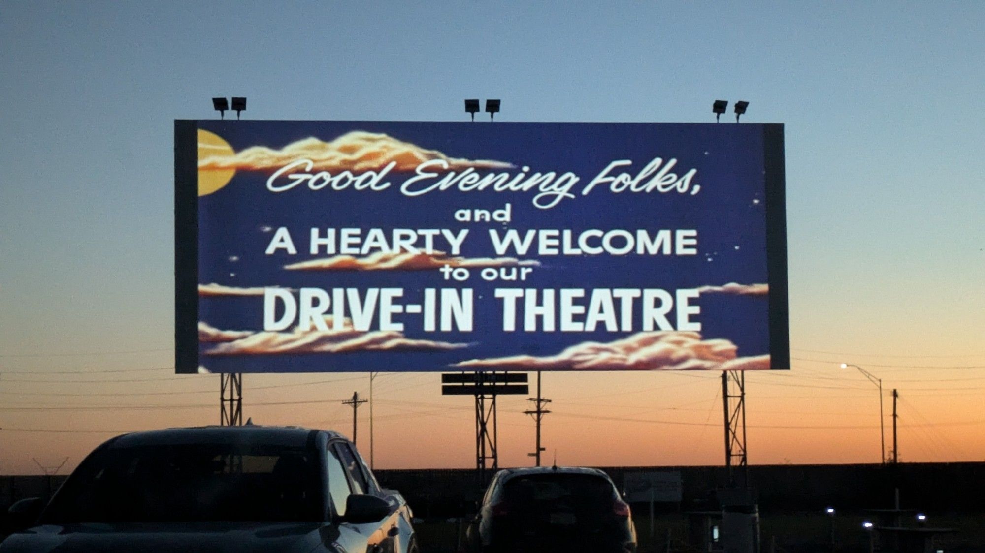 A drive in theater sign that reads "Good evening folks and a hearty welcome to our drive in theater"