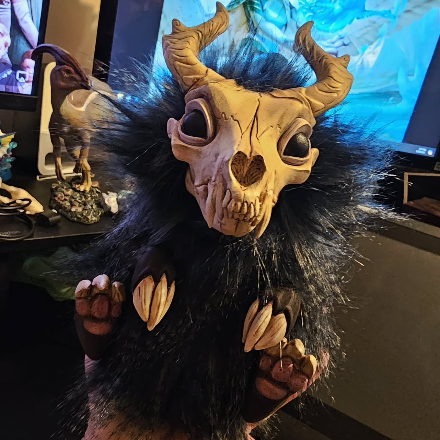 A sculpture of a fluffy black creature with a dog skull and horns, and large clawed paws. Sitting in persons hand.