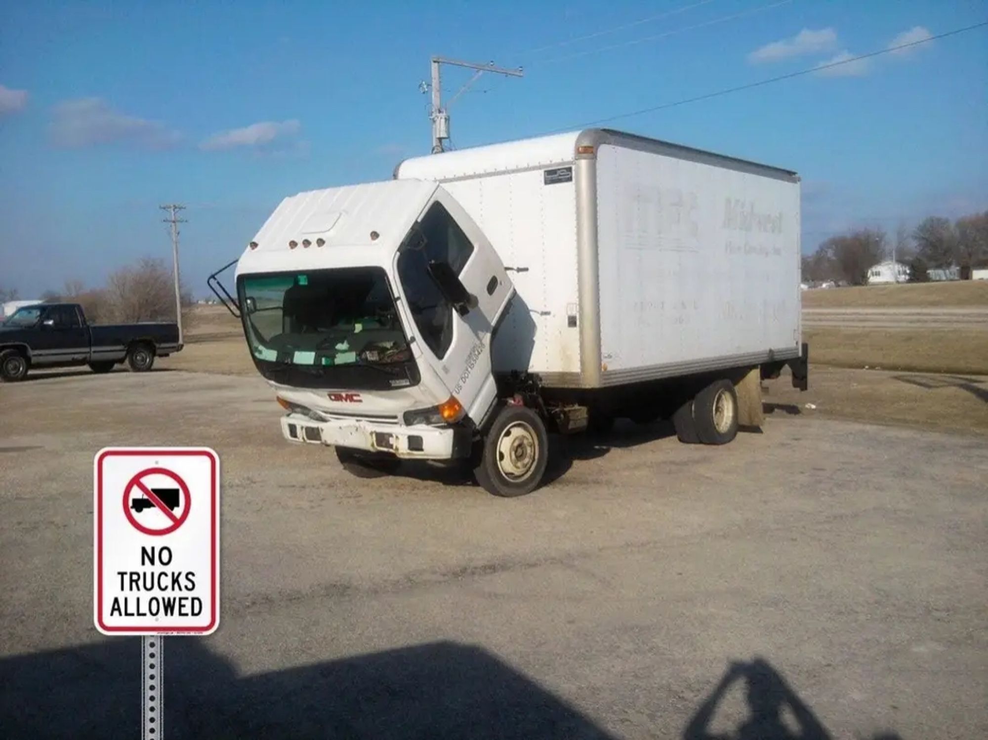 A white panel truck with the cab tipped forward.
In the foreground is a warning sign. NO TRUCKS ALLOWED.