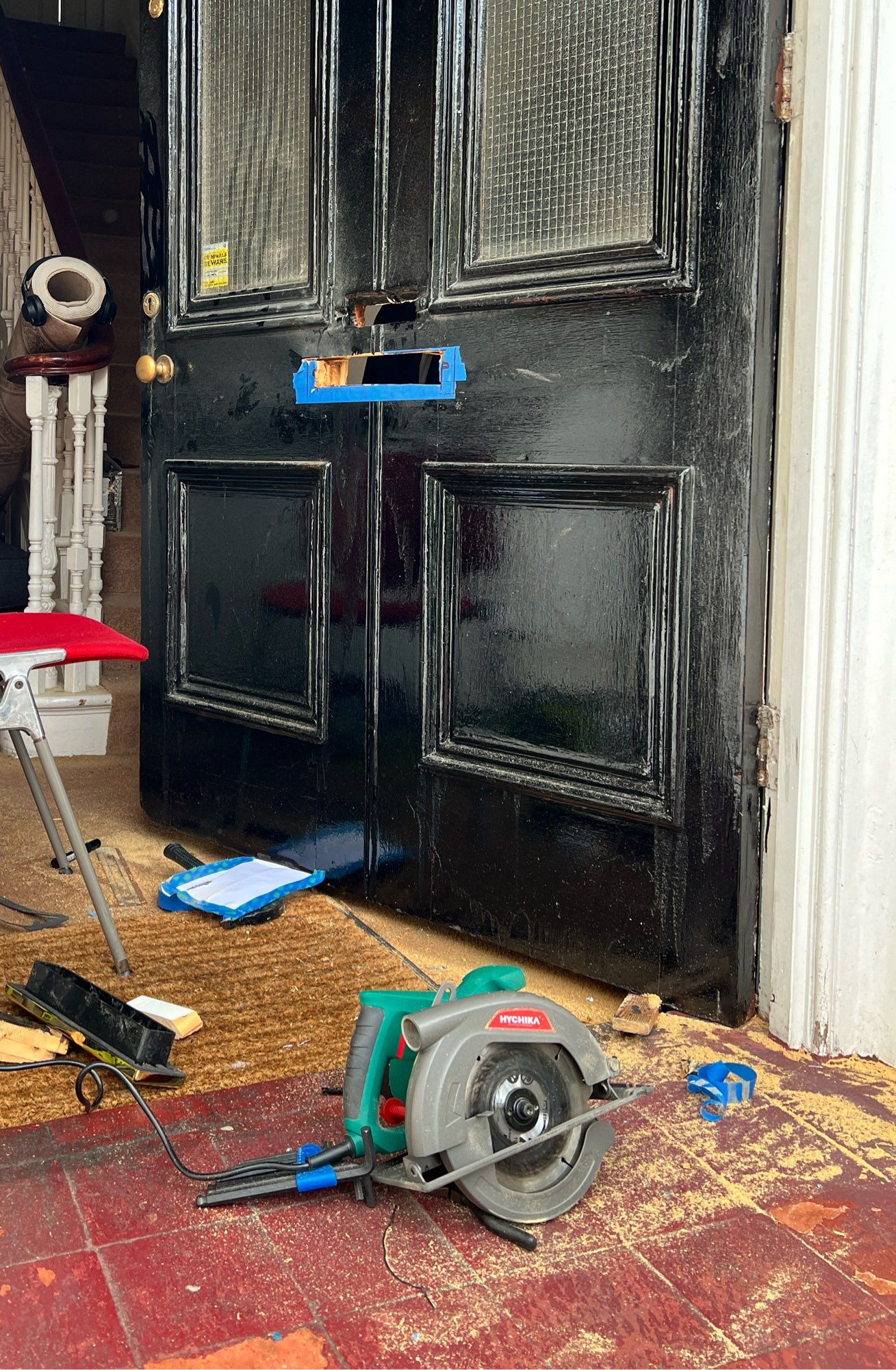 A door with a horizontal slot cut into it, the edges of the hole marked out by blue masking tape (which is partially chopped into). Sawdust everywhere. The saw is resting in the foreground on the floor